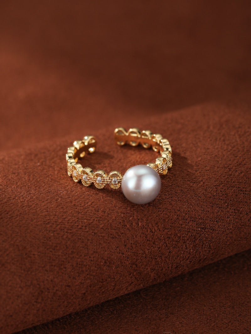 Gold-toned open cuff ring with a single silver freshwater pearl and small sparkling accents on the band.