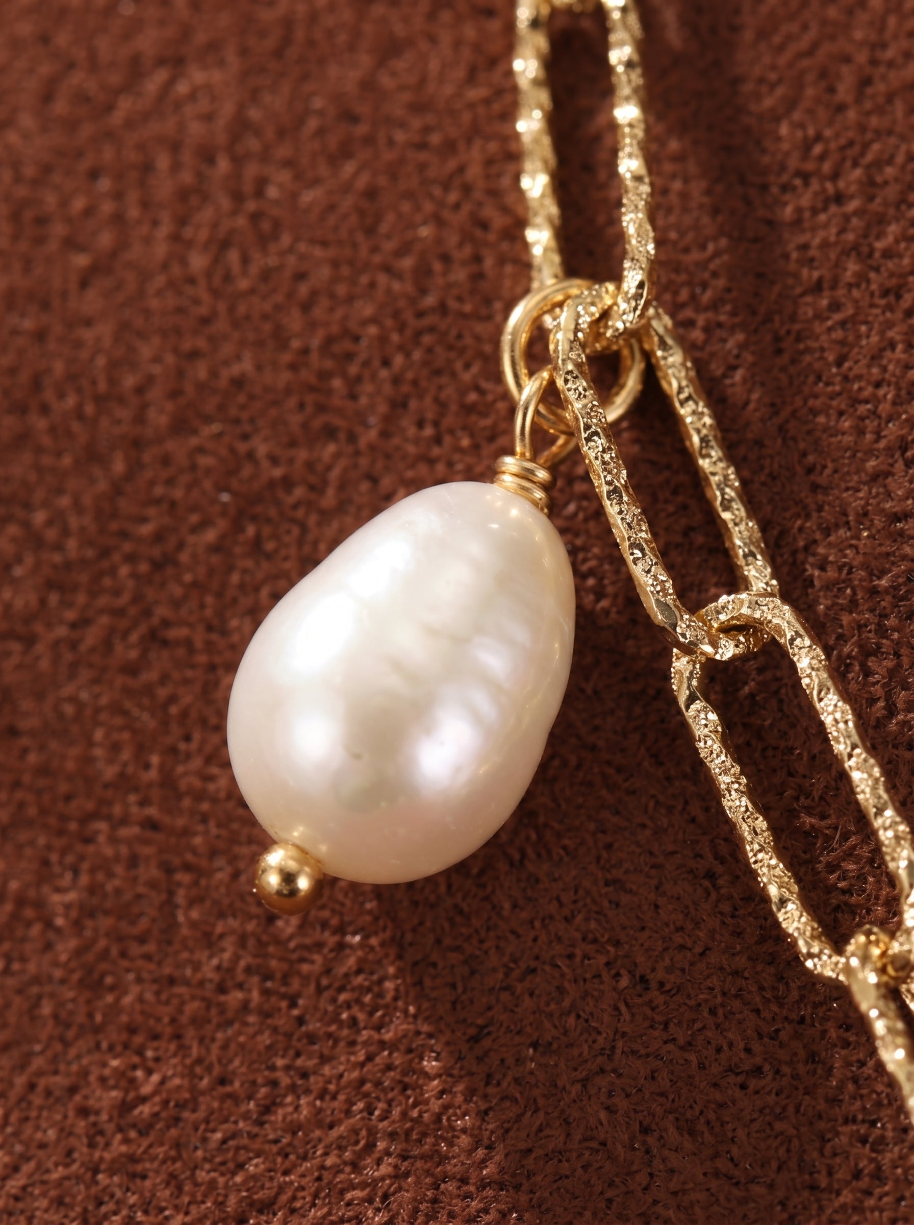 Gros plan d'un collier à chaîne à maillons imposants texturés dorés avec un seul et lustré pendentif en perle goutte blanche d'eau douce. @pearl