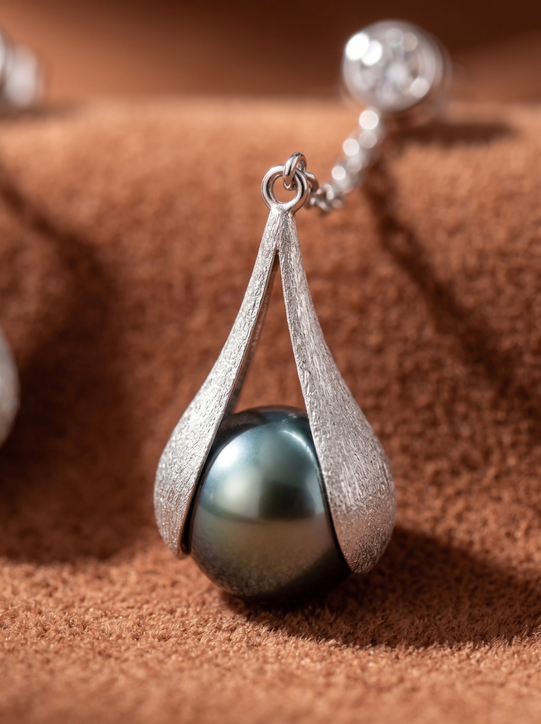 Close-up of Enfold Tahitian Pearl Drop Earrings featuring a lustrous 10mm round black pearl cradled in a textured silver-tone setting with a clear stone stud. @pearl