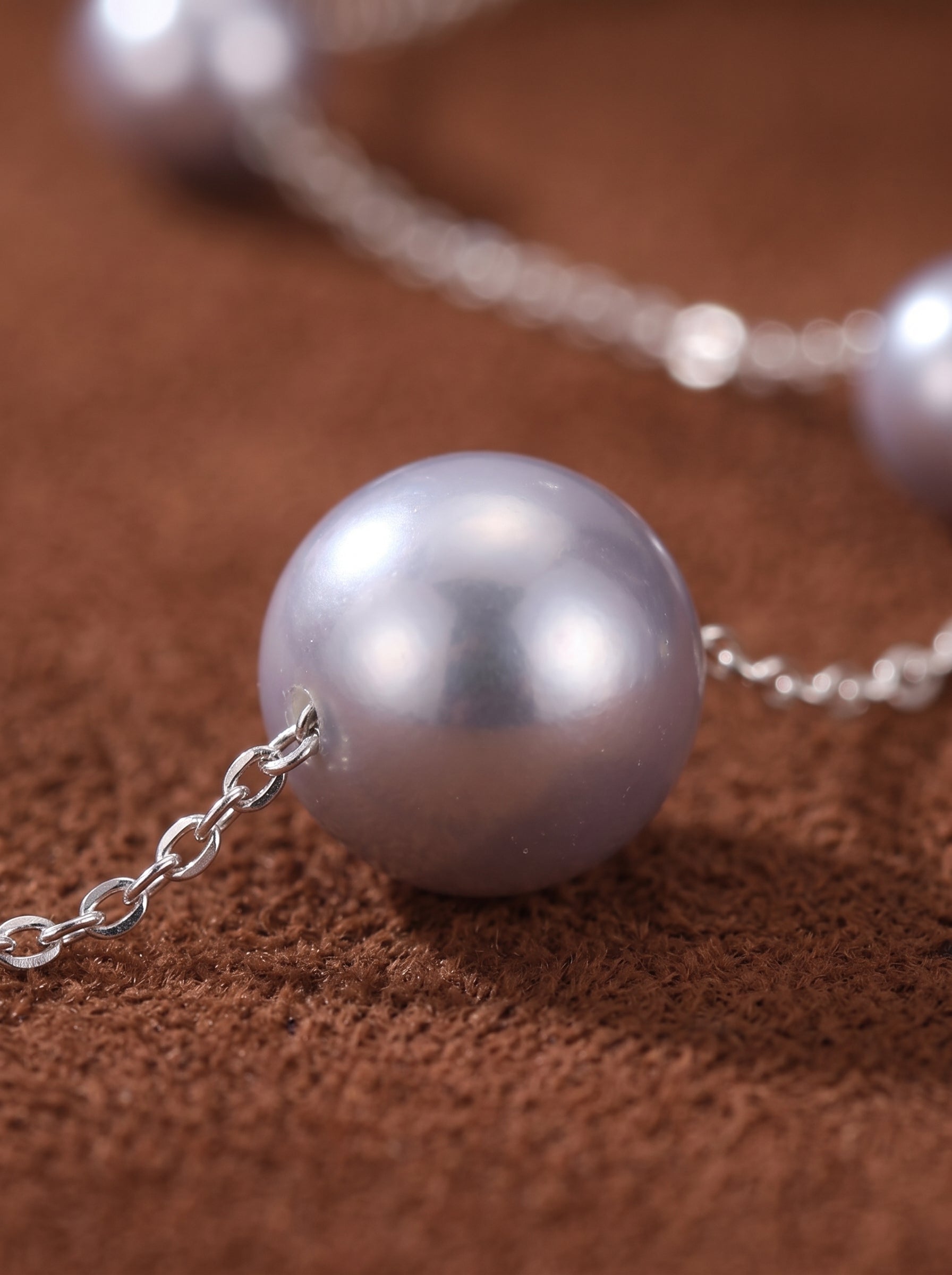 Close-up of the Enigma Akoya Pearl Spaced Choker Necklace, featuring lustrous, round grey pearls spaced along a delicate silver chain against a brown textured background. @pearl