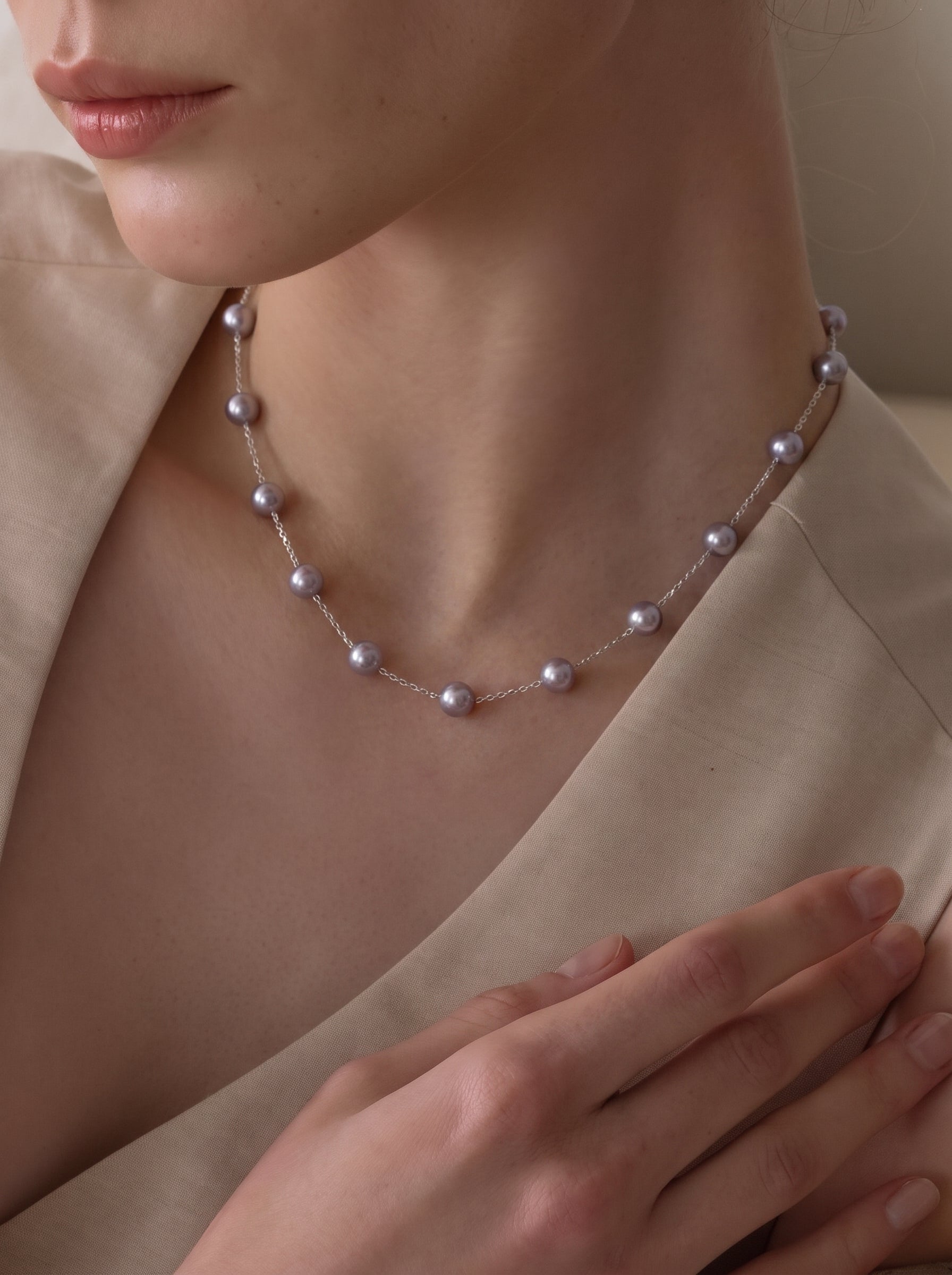 A close-up shot of a woman wearing the Enigma Akoya Pearl Spaced Choker Necklace, showcasing the delicate chain and lustrous pearls against a neutral-colored top. @model