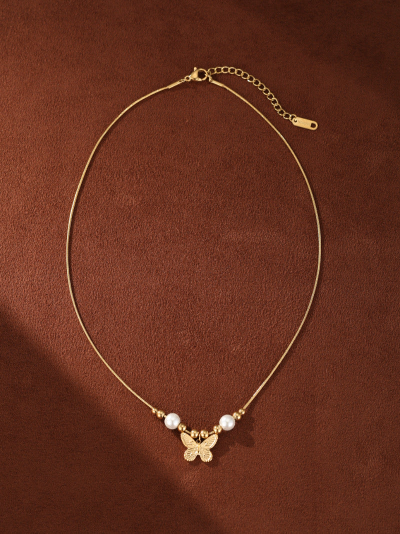 Délicat collier à chaîne dorée avec un pendentif papillon texturé, accentué de deux perles blanches d'eau douce et de petites perles dorées.