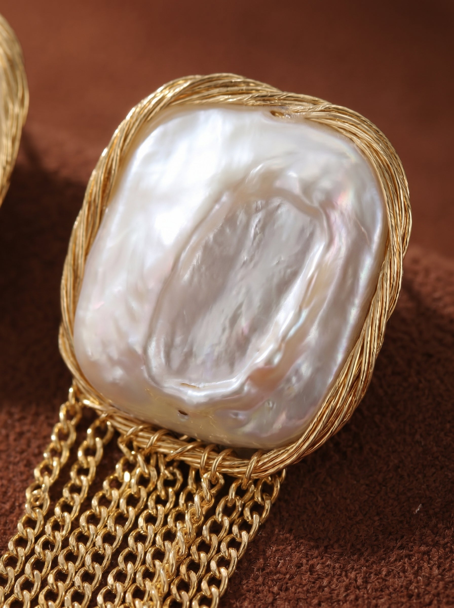 Close-up of Epoch Fringe earrings showcasing a large, irregular freshwater baroque pearl with a lustrous white sheen, set in a twisted gold-toned wire frame. A delicate fringe of gold chains dangles below the pearl. @pearl