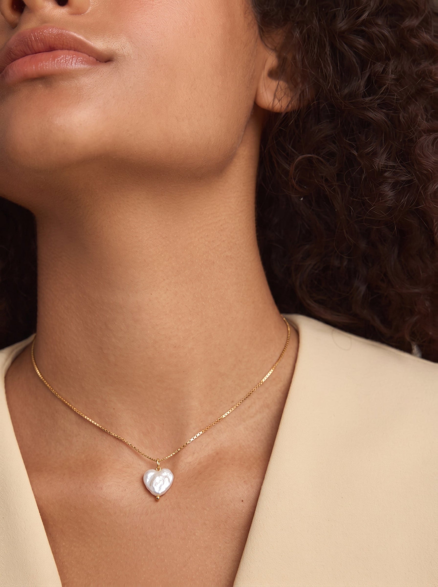 Gros plan d'une mannequin portant un collier à chaîne dorée avec une seule et irrégulière perle blanche d'eau douce en forme de cœur. @model