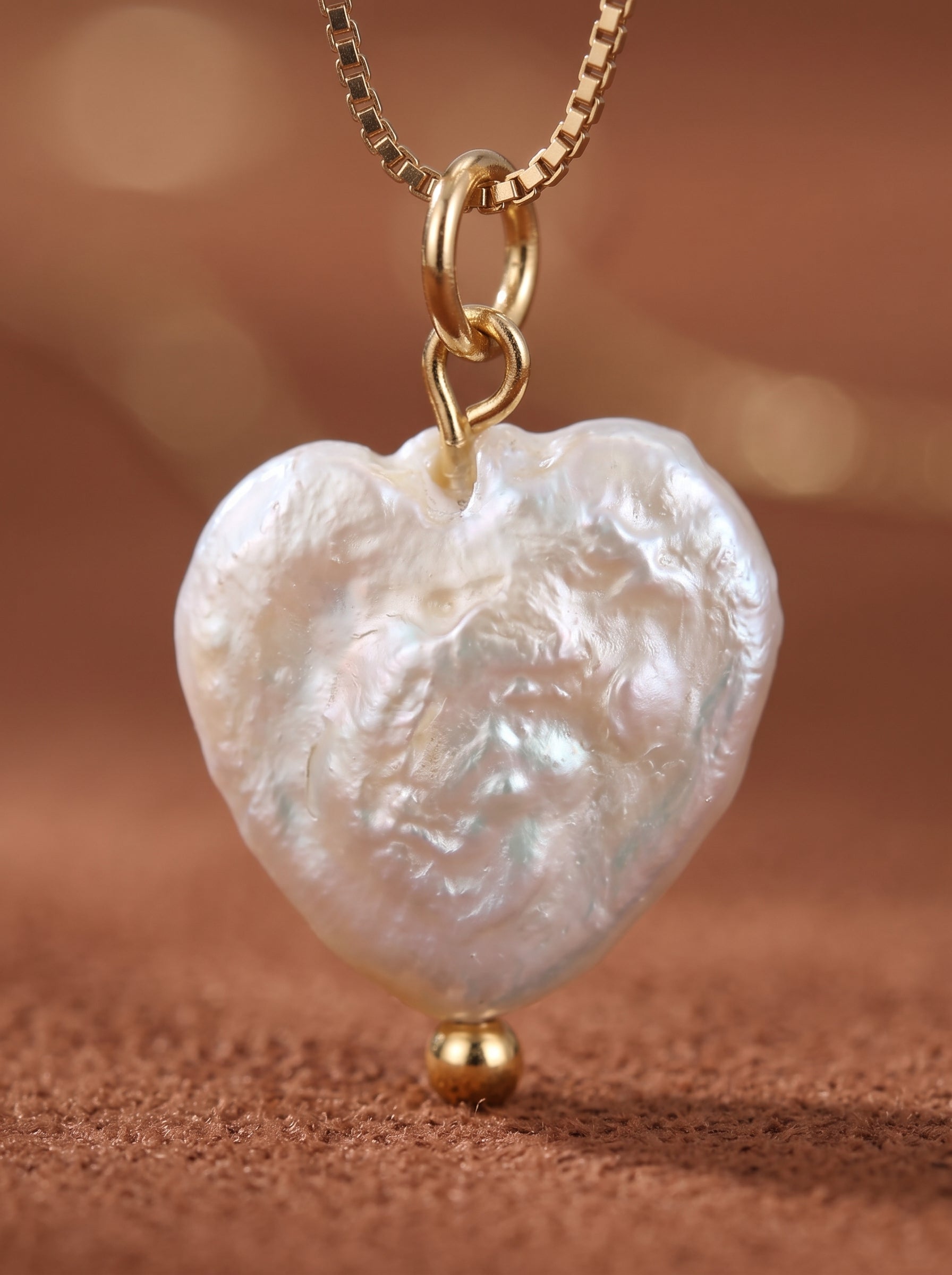 Gros plan d'un pendentif cœur en perle baroque blanche d'eau douce sur une délicate chaîne dorée, accentué d'une petite perle dorée en bas. @pearl