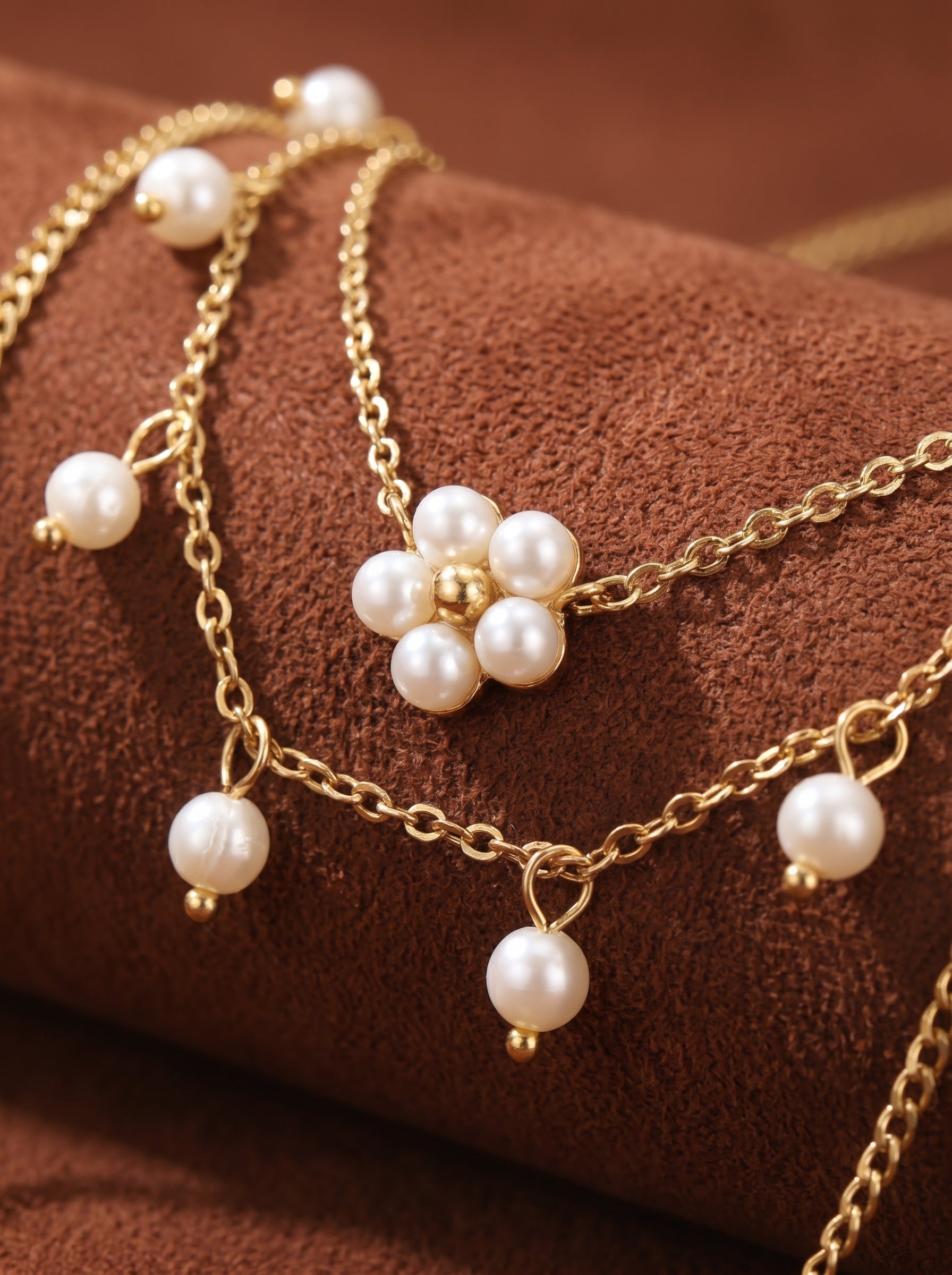 Close-up of a gold-toned layered chain necklace featuring a delicate flower motif made of 4mm round white freshwater pearls and smaller dangling pearls.
