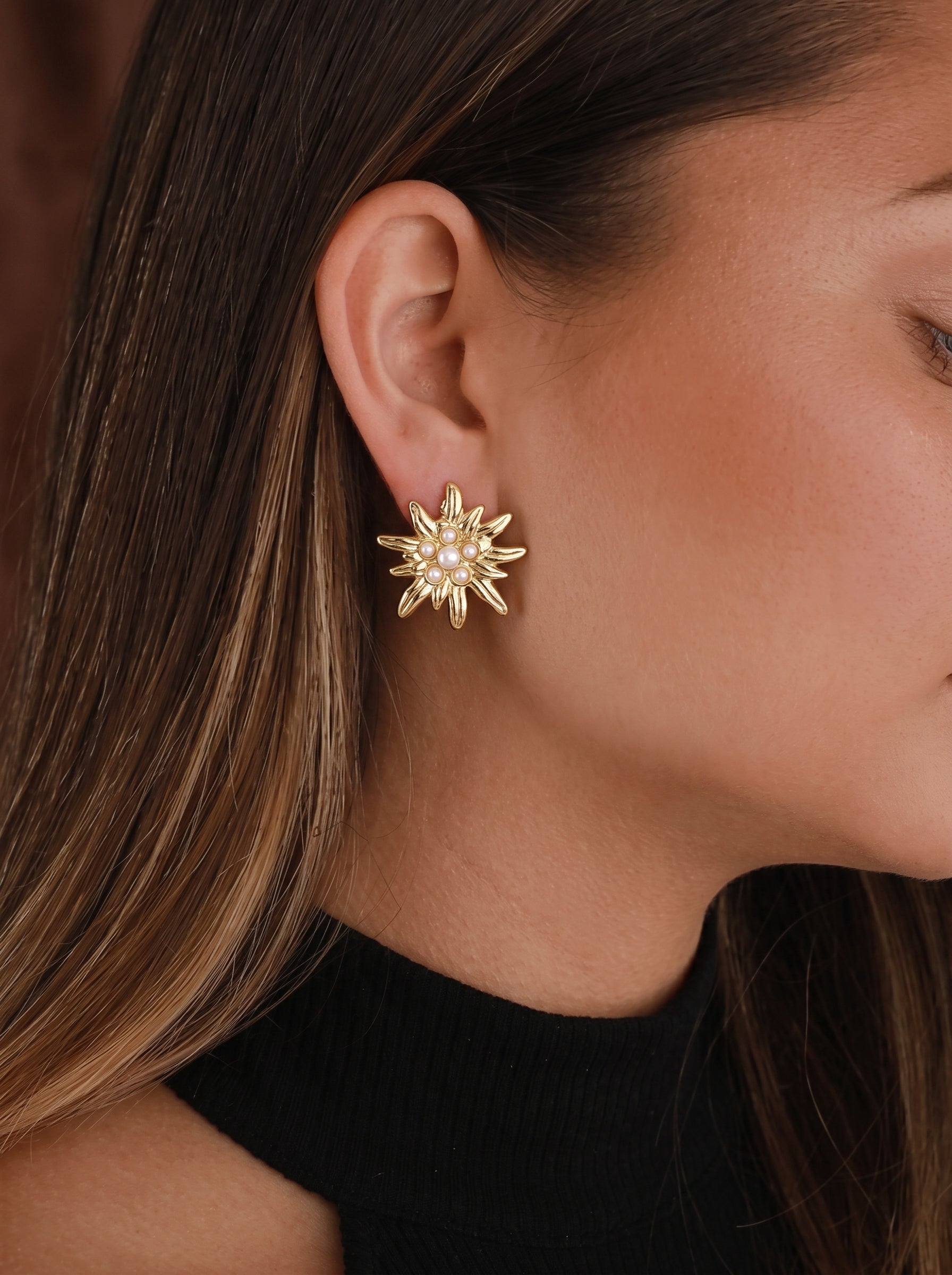 Boucles d'oreilles puces ton or en forme de soleil avec une perle imitation centrale entourée de plus petites perles, portées par une mannequin. @model