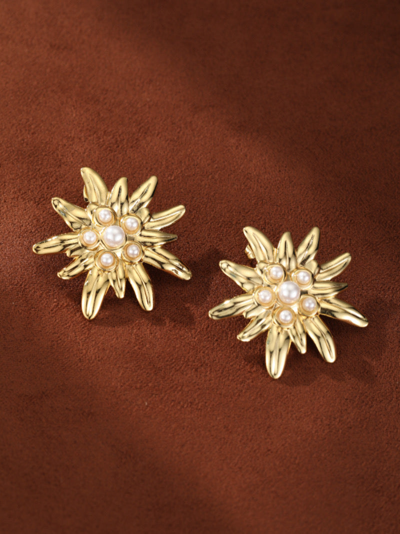 Gold-toned flower stud earrings featuring a central 6mm imitation pearl surrounded by smaller 3mm imitation pearls, set on a brown textured background.