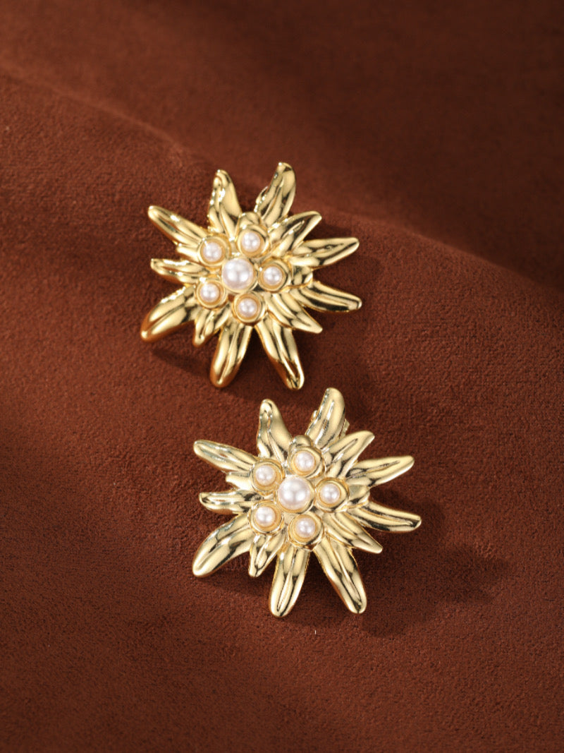 Flare imitation pearl flower stud earrings in gold tone with a central 6mm button pearl surrounded by smaller 3mm pearls on a brown textured background.