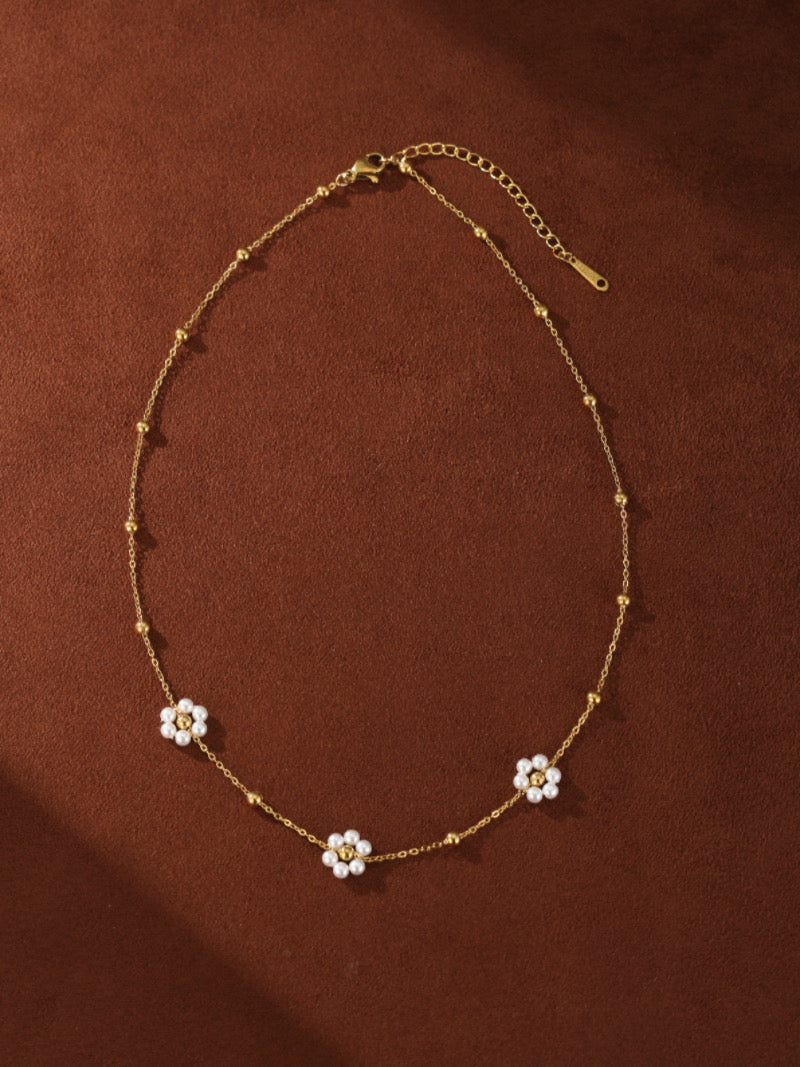 A delicate gold-toned necklace featuring a thin chain adorned with small golden beads and four flower charms. Each flower is made of tiny white pearls with a small golden bead in the center, showcasing a floating layered design.
