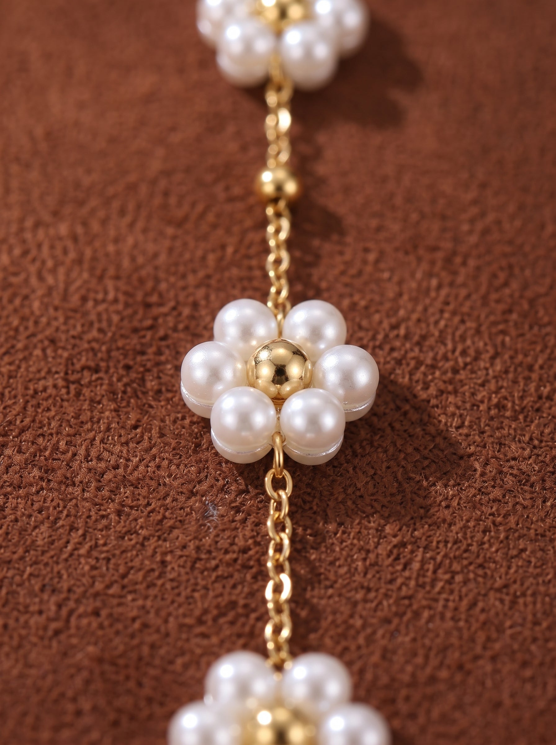 Close-up of a delicate gold chain necklace adorned with small white freshwater pearl flowers, each with a golden bead center. The necklace is laid on a textured brown background. @pearl