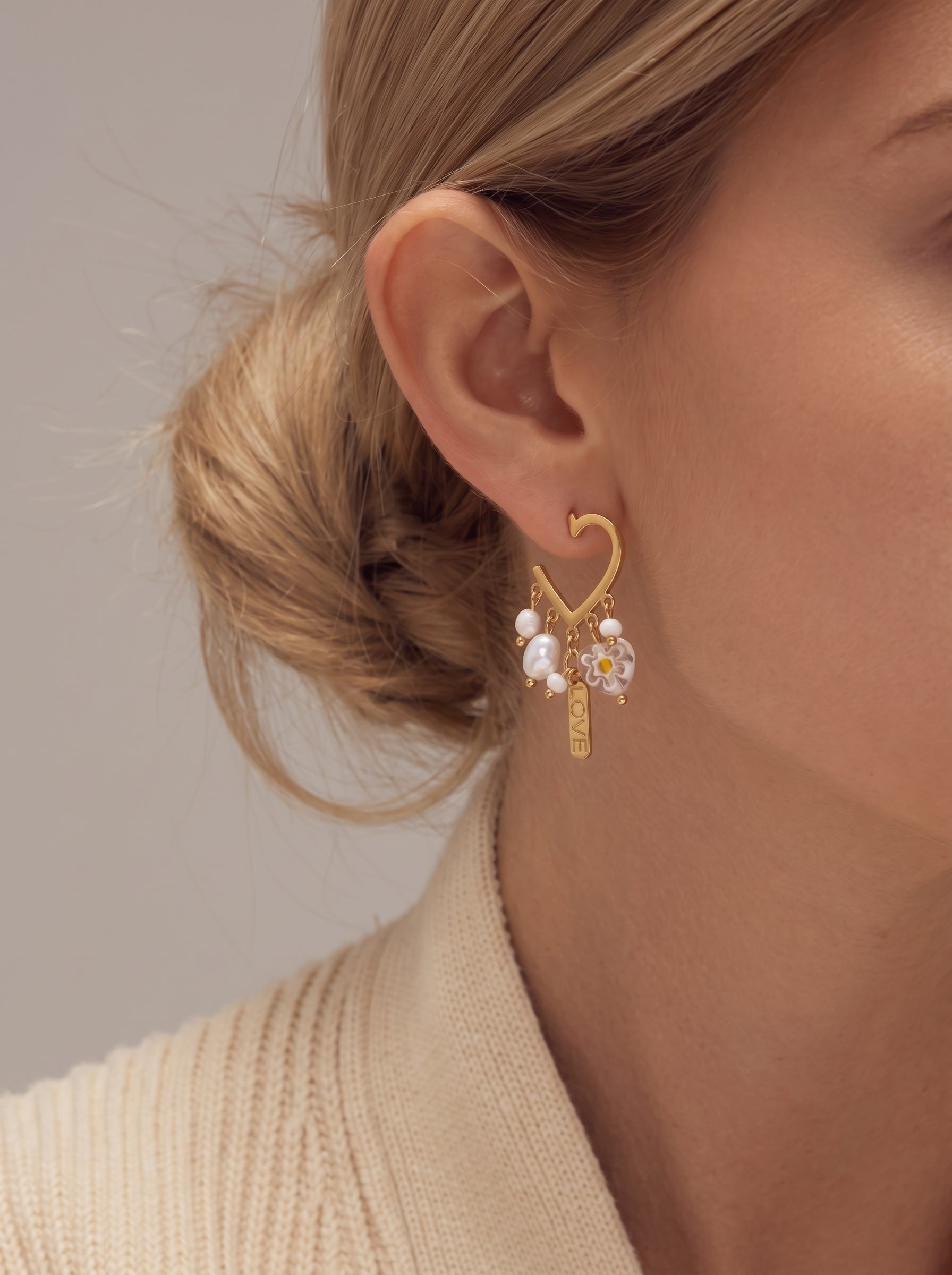 Boucles d'oreilles goutte cœur Fleurish en perle d'eau douce présentant un cadre cœur doré avec des perles blanches pendantes, des perles florales, et une breloque « LOVE », portées par une mannequin @model