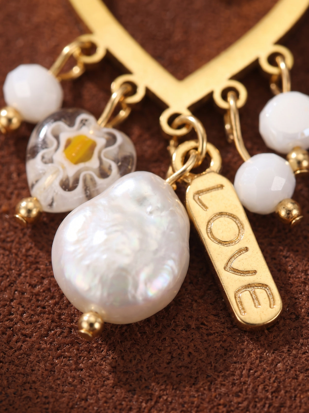 Gros plan des boucles d'oreilles pendantes cœur Fleurish en perle d'eau douce, présentant un cadre cœur doré avec des perles baroques et bouton pendantes en eau douce, des perles à motif floral, et une breloque « LOVE ». @pearl
