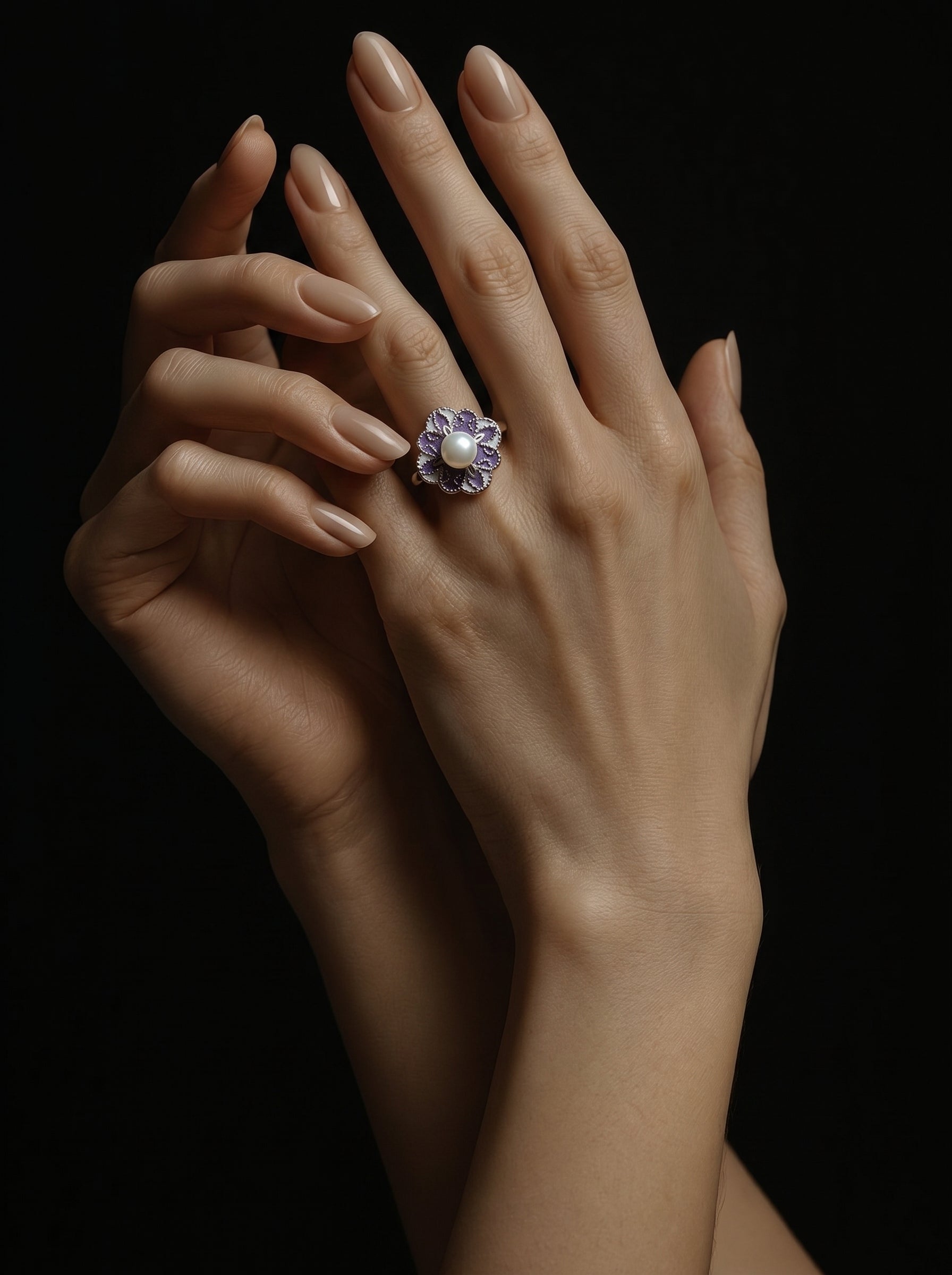Bague manchette florale Flora en perle d'eau douce présentant une délicate fleur émaillée violette avec une lumineuse perle blanche d'eau douce en son centre, à la main d'une femme contre un fond sombre. @model