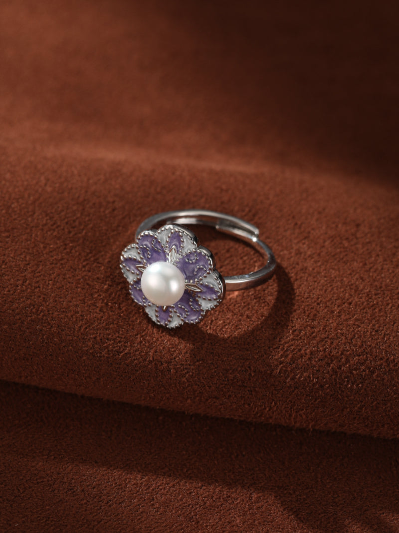 Flora - Freshwater Pearl Flower Cuff Ring with a purple enameled flower motif and a lustrous white freshwater pearl at its center, set on an adjustable silver band against a brown textured background. #model