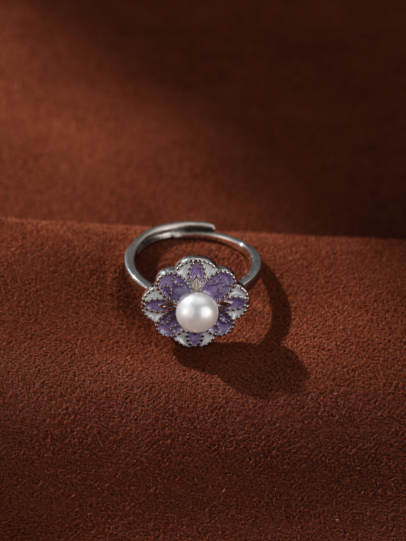 Flora - Freshwater Pearl Flower Cuff Ring featuring a purple and white enameled flower design with a central white freshwater pearl, set against a textured brown background.
