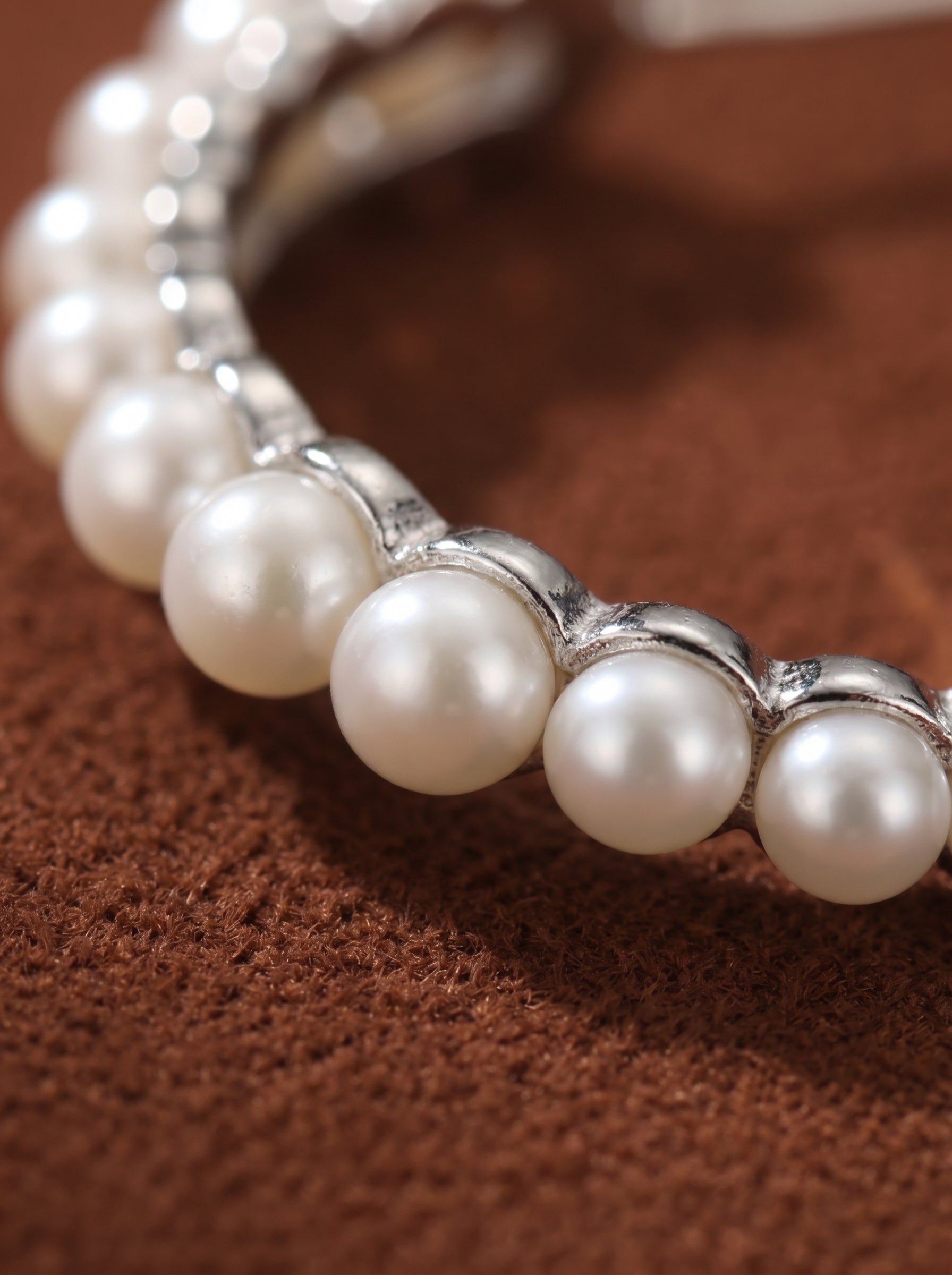 Close-up of the "Flow" freshwater pearl long dangle earrings, showcasing luminous white pearls set in silver on a textured brown background. @pearl
