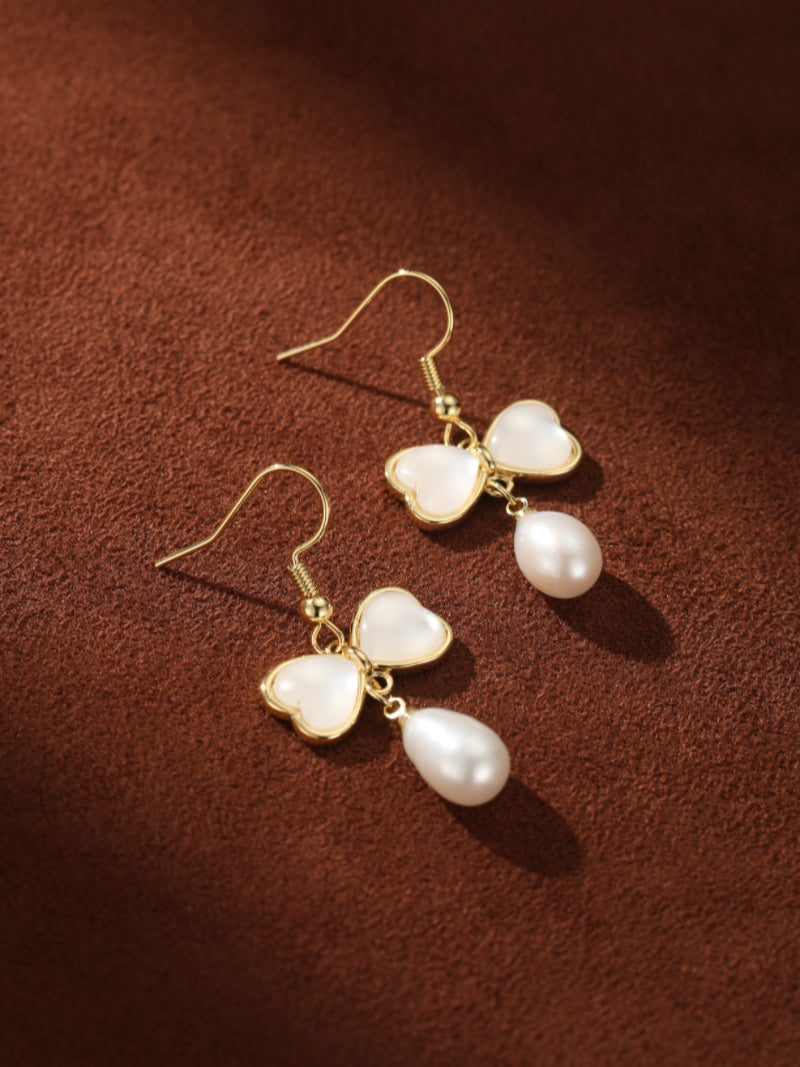 Boucles d'oreilles pendantes ton or présentant une breloque papillon faite de deux pierres blanches en forme de cœur, suspendant une perle en larme d'eau douce.