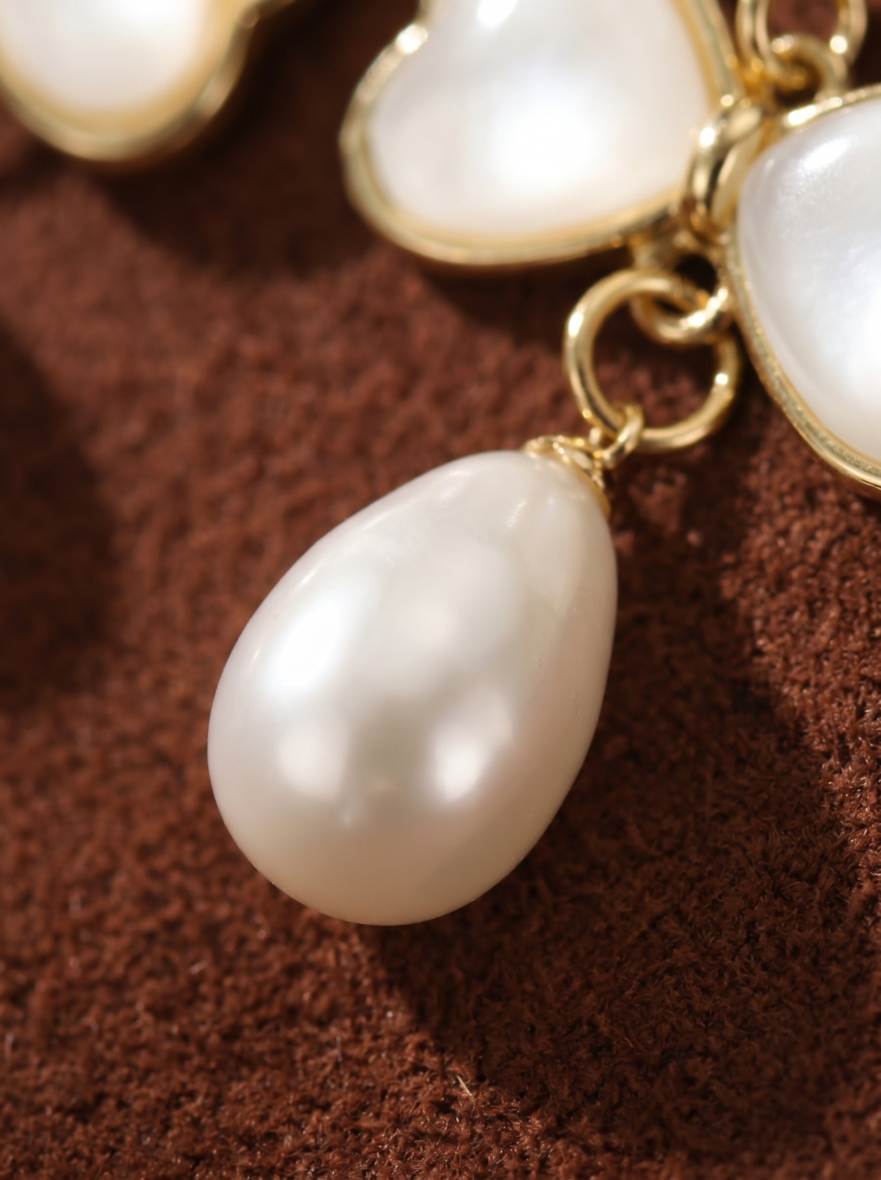Close-up of Flutter Freshwater Pearl Butterfly Dangle Earrings featuring a teardrop-shaped white pearl suspended from a gold-tone butterfly charm with heart-shaped wings, set against a textured brown background. @pearl