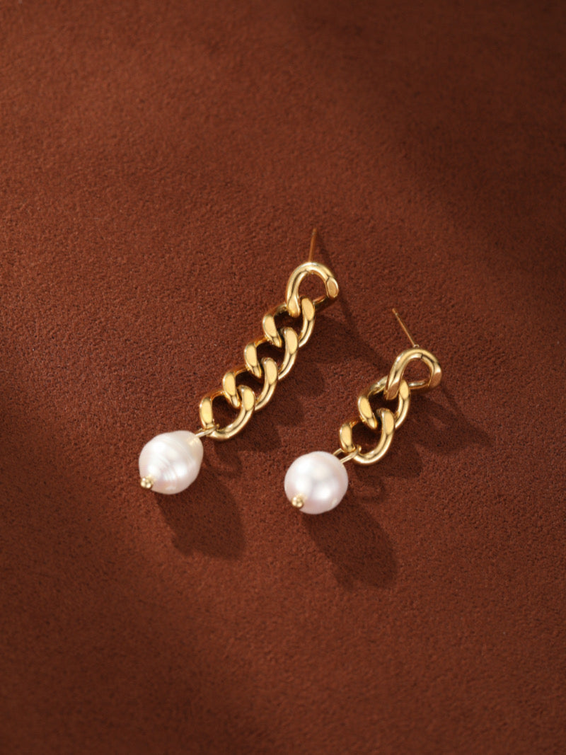 Gold-toned chain dangle earrings featuring white freshwater seed pearls, presented on a textured brown background.