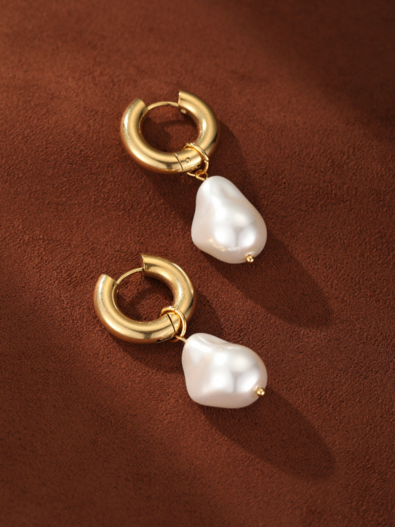 Forma chunky gold hoop dangle earrings featuring unique freshwater baroque pearls on a brown background.