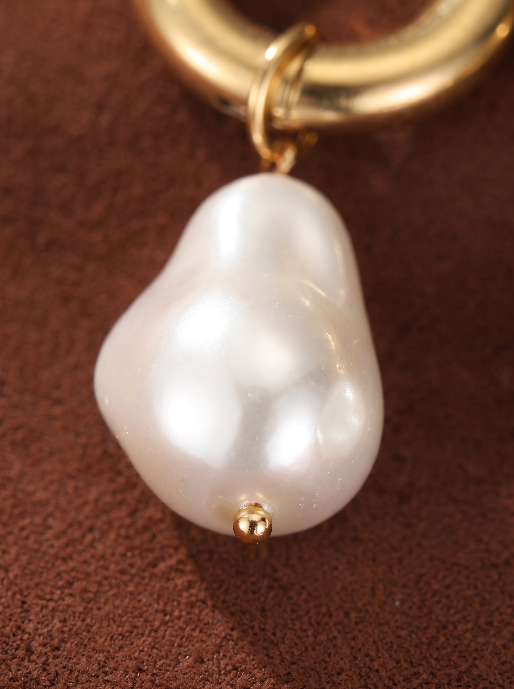 Close-up of a white baroque freshwater pearl dangling from a gold-toned chunky hoop earring, showcasing its unique shape and luminous finish. @pearl