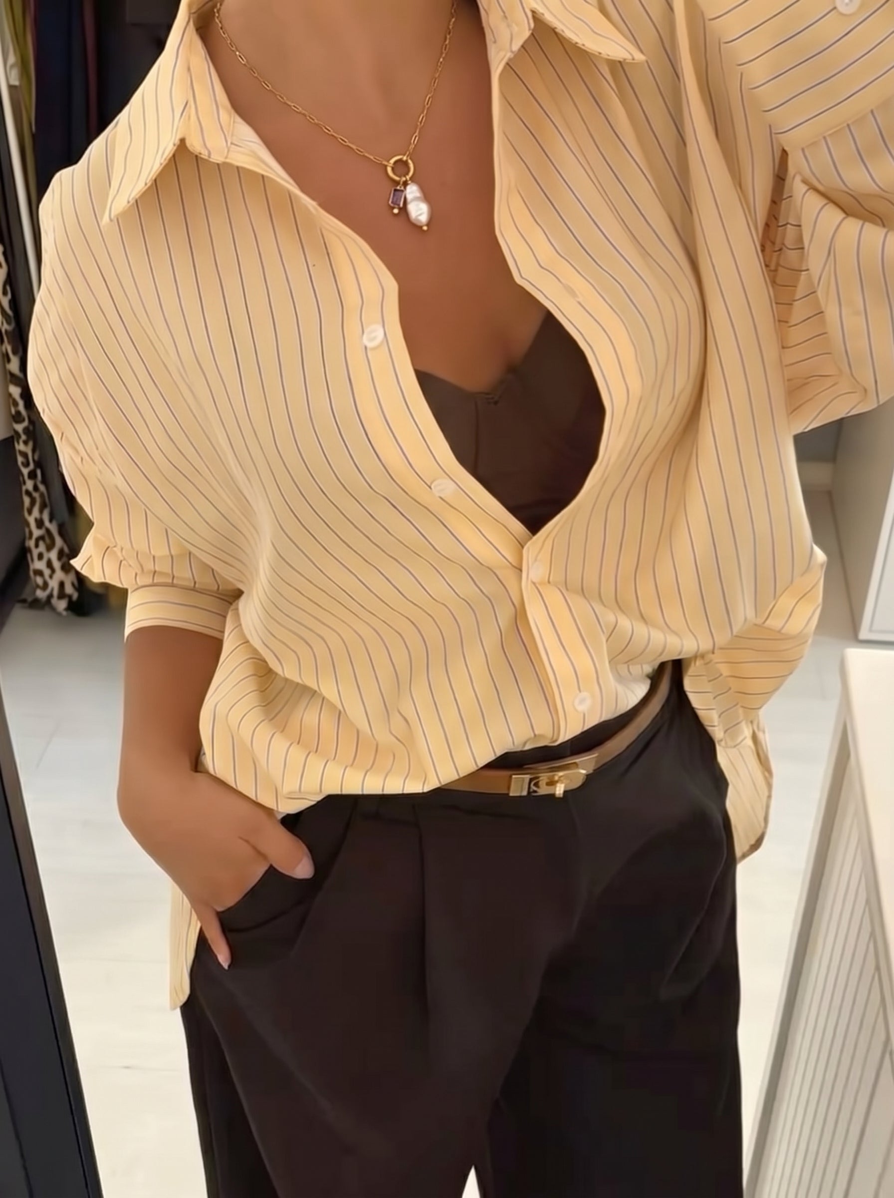 Une femme en chemise rayée jaune et pantalon noir porte un collier doré avec une perle baroque d'eau douce et une pierre gemme violette. @lifestyle