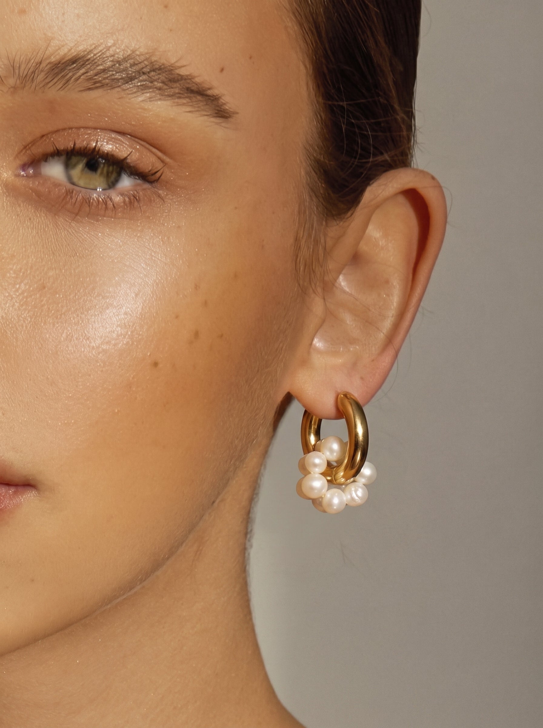 Gros plan du lobe d'oreille d'une femme portant une créole dorée ornée d'un groupe de petites et lumineuses perles blanches d'eau douce. @model