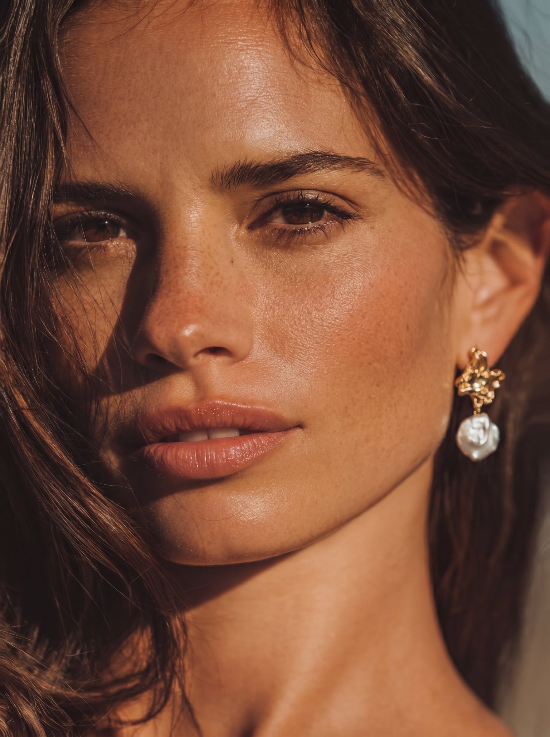 Close-up of a woman's face showcasing the Gilded Wave Freshwater Pearl Drop Earrings, featuring an organic gold-toned top and a large, irregularly shaped pearl drop. @model