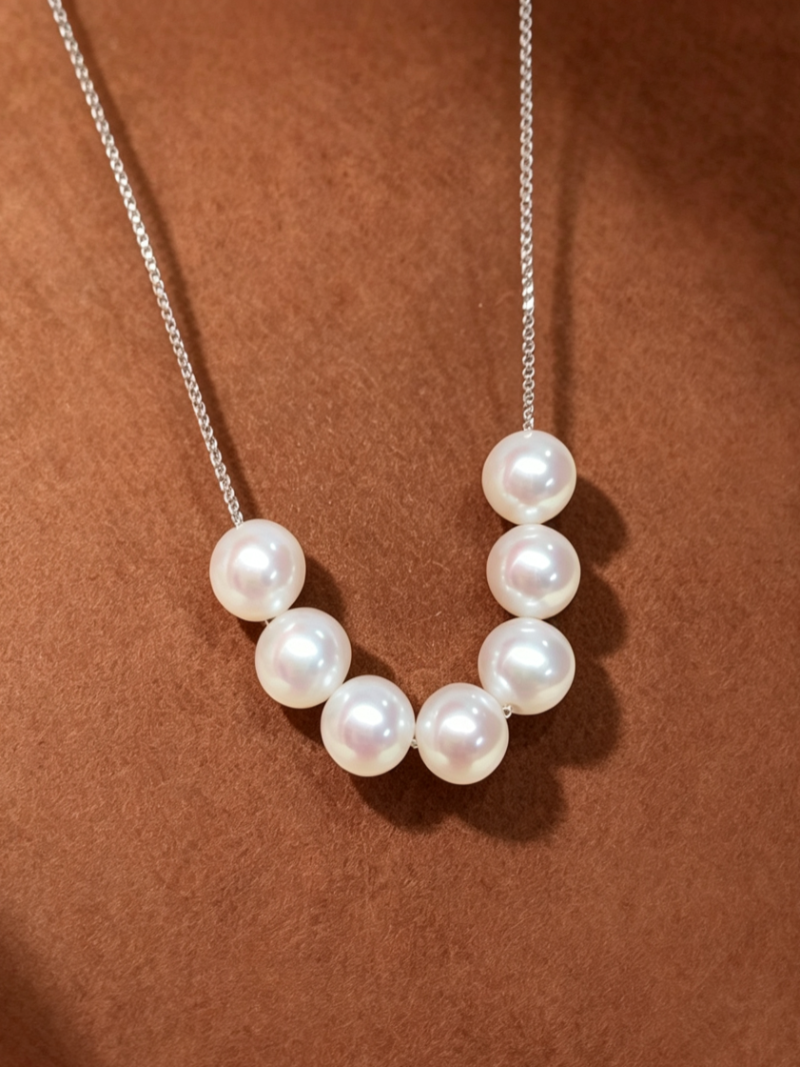 A delicate silver chain necklace featuring seven lustrous 6mm white freshwater pearls spaced evenly to create a floating effect on a brown textured background.