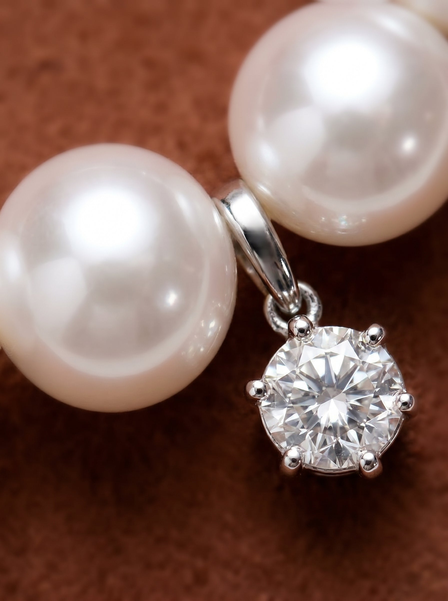 Close-up of a Gleam Curve necklace featuring a sparkling diamond pendant suspended between two lustrous white freshwater pearls on a brown background. @pearl