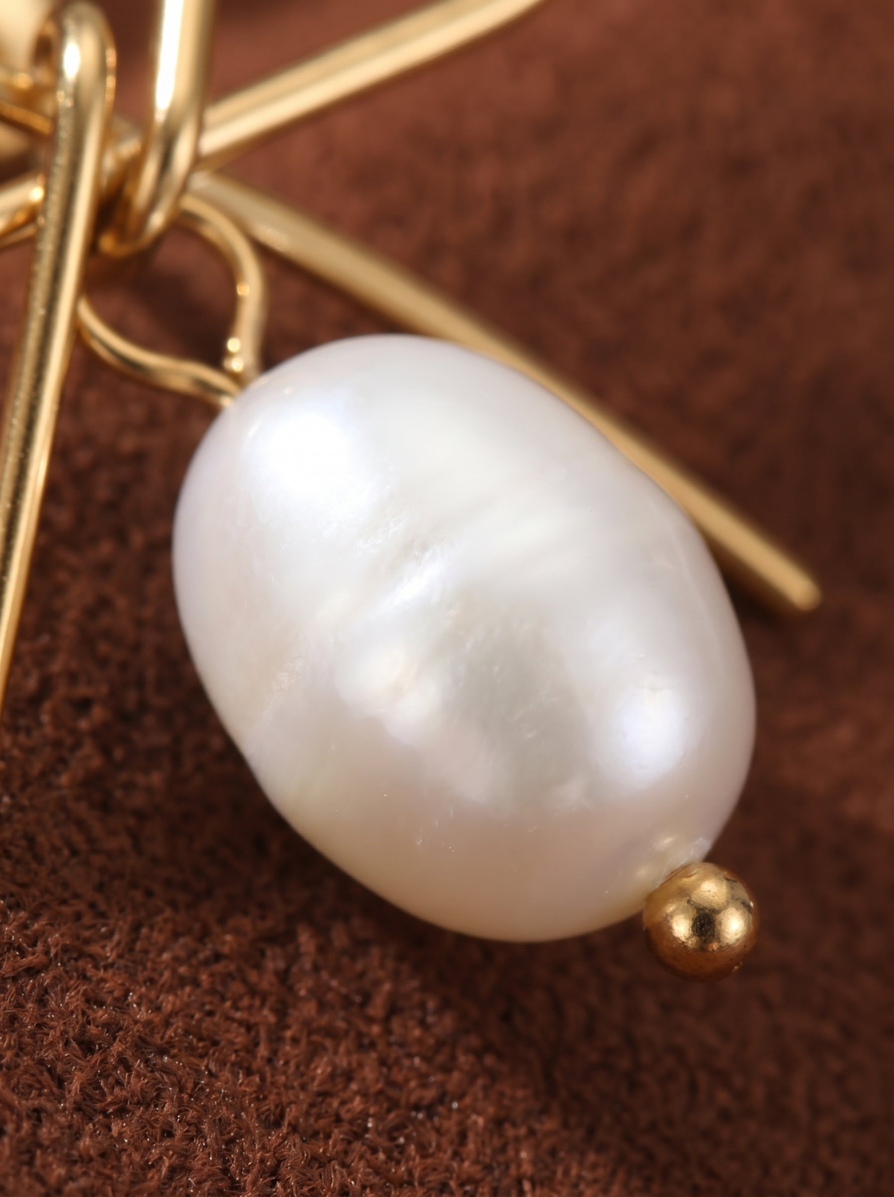Glimmer - Freshwater Pearl Bow Stud Earrings featuring a gold-tone bow design suspending a lustrous white baroque freshwater pearl, set against a brown textured background. @pearl