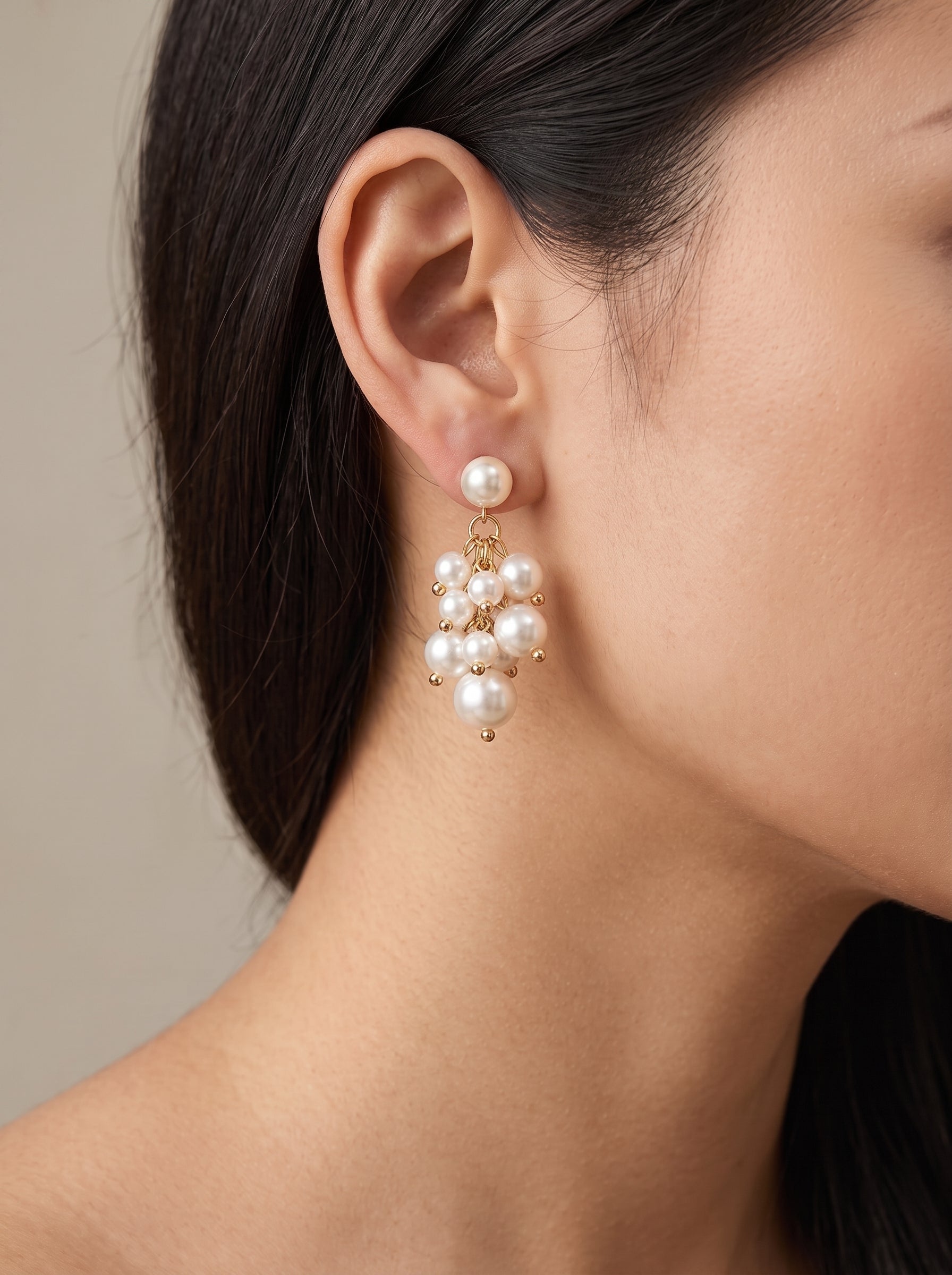 Gros plan de l'oreille d'une femme portant les boucles d'oreilles pendantes en grappe Glow Orb en perle d'eau douce, présentant une puce dorée avec une seule perle et une grappe cascadante de plus petites perles blanches accentuées de perles dorées. @model