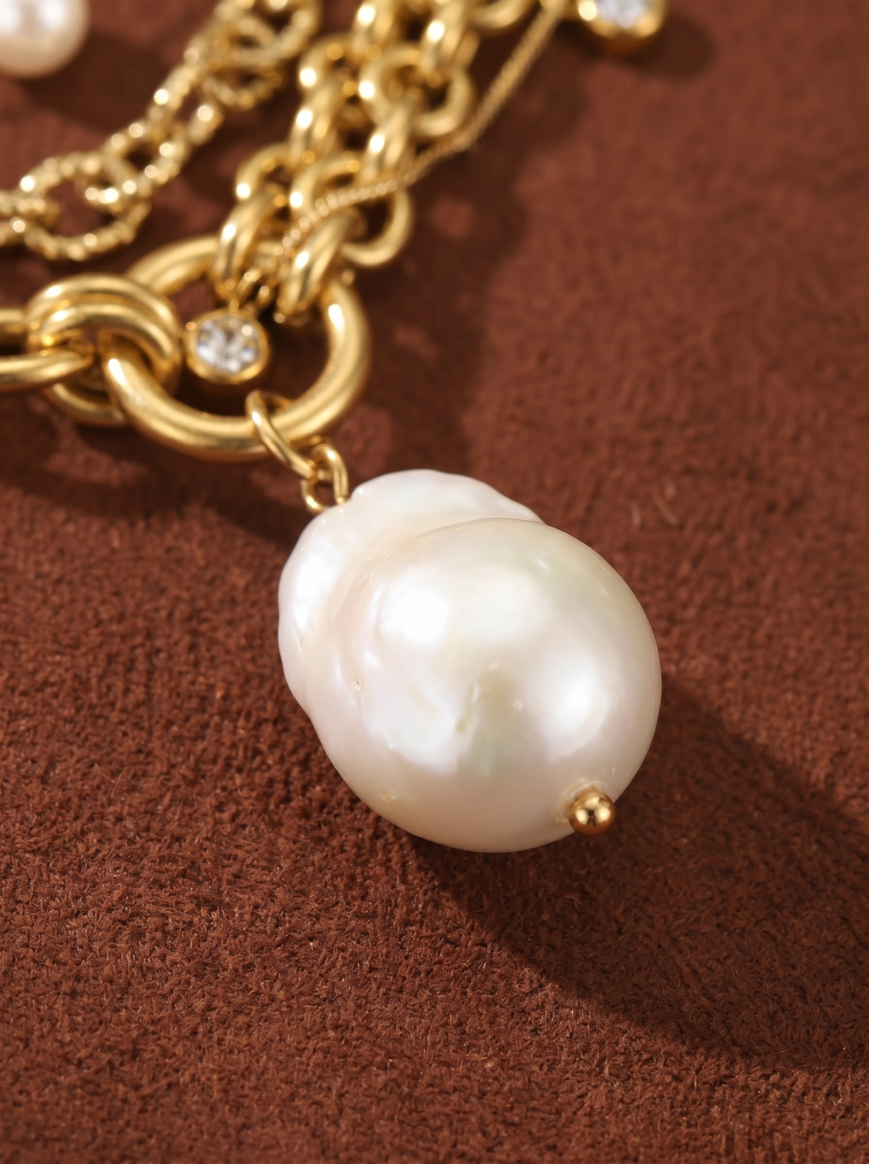 Close-up of a layered gold necklace featuring small white freshwater pearls and a large baroque freshwater pearl pendant with cubic zirconia accents.@pearl