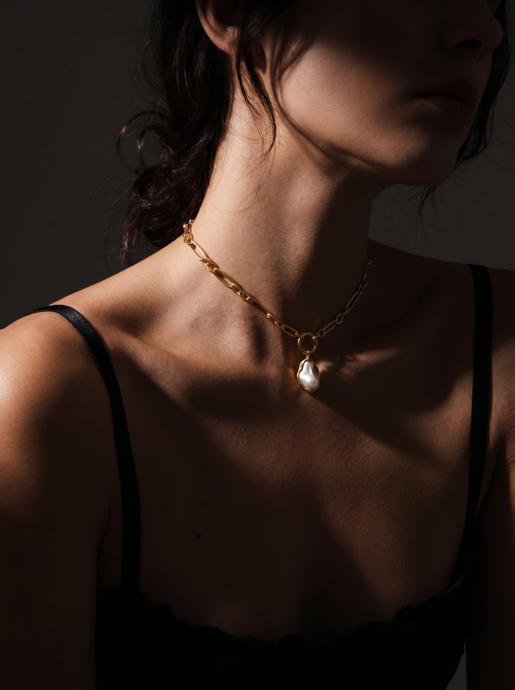 Close-up of a woman wearing the Golden Tide chunky gold chain necklace with a large, irregular white freshwater pearl pendant. @model