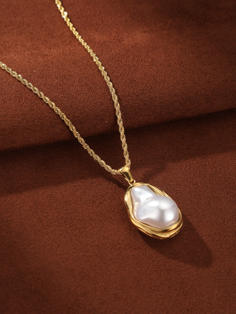 Golden Tide chunky gold-toned chain necklace featuring a large, irregular white freshwater pearl pendant set in a fluid gold frame, displayed on a textured brown background. @pearl