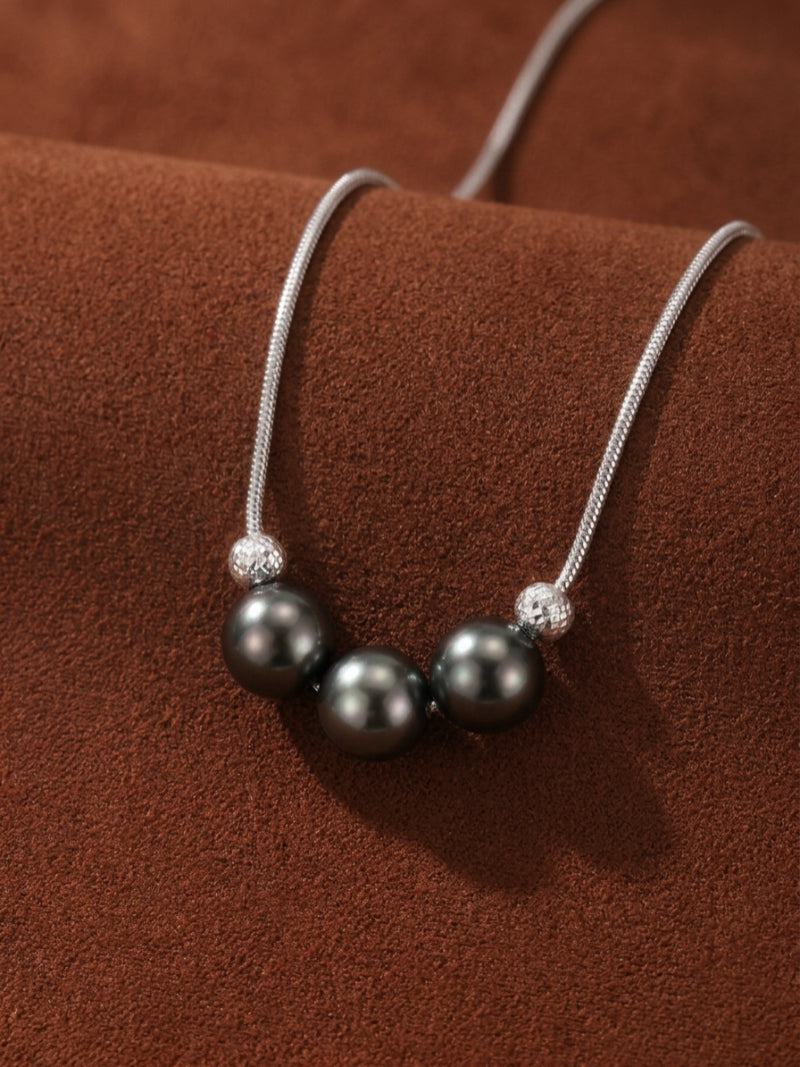Grit Tahitian Pearl Pendant Necklace featuring three 9mm round Tahitian black pearls separated by textured silver beads on a snake chain, displayed on a brown textured background.