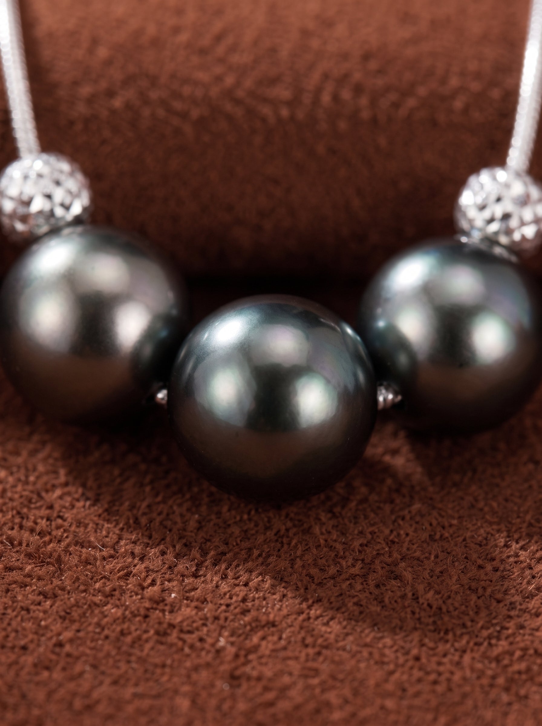 Grit necklace featuring three round Tahitian black pearls separated by textured silver beads, on a brown textured background. @pearl
