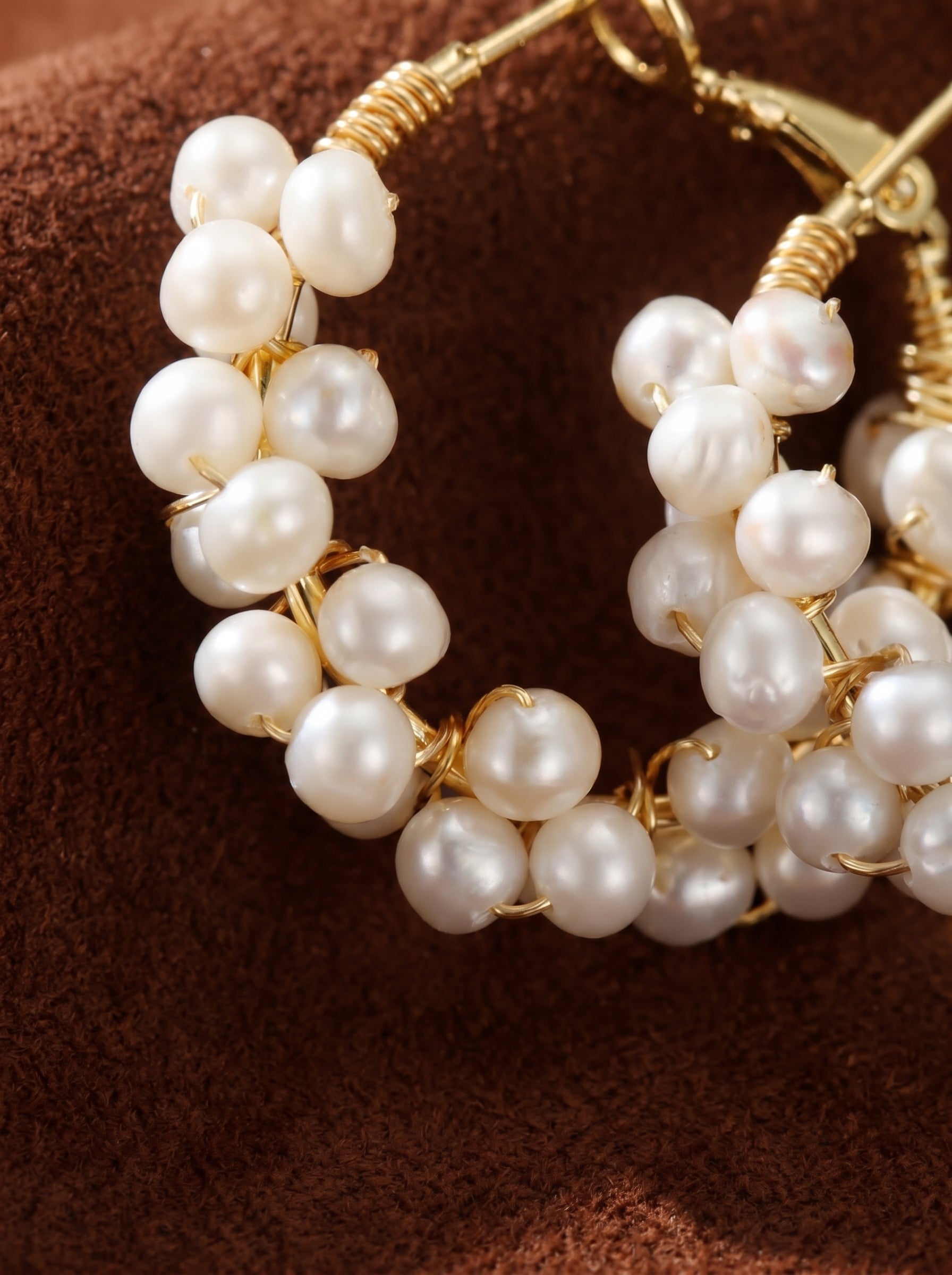 Close-up of Grove Freshwater Pearl Hoop Drop Earrings, featuring clusters of luminous white seed pearls wrapped around gold-toned hoops.@pearl