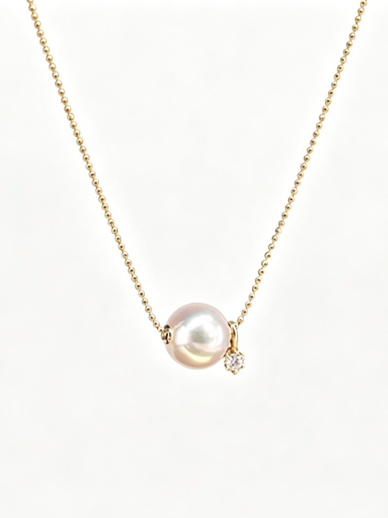 A close-up studio shot of a Halo Akoya Pearl Star Floating Necklace on a white background. The necklace features a single, lustrous 8mm Akoya pearl with soft pink and white overtones, suspended on a delicate gold chain. A small, sparkling diamond star accent dangles beside the pearl. The floating design allows the pearl to rest gracefully. @perle