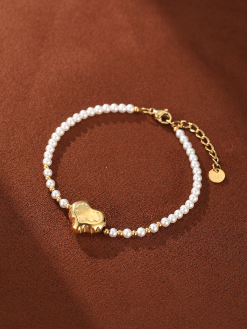 Freshwater pearl beaded bracelet with a gold-toned heart charm in the center, set against a brown background.