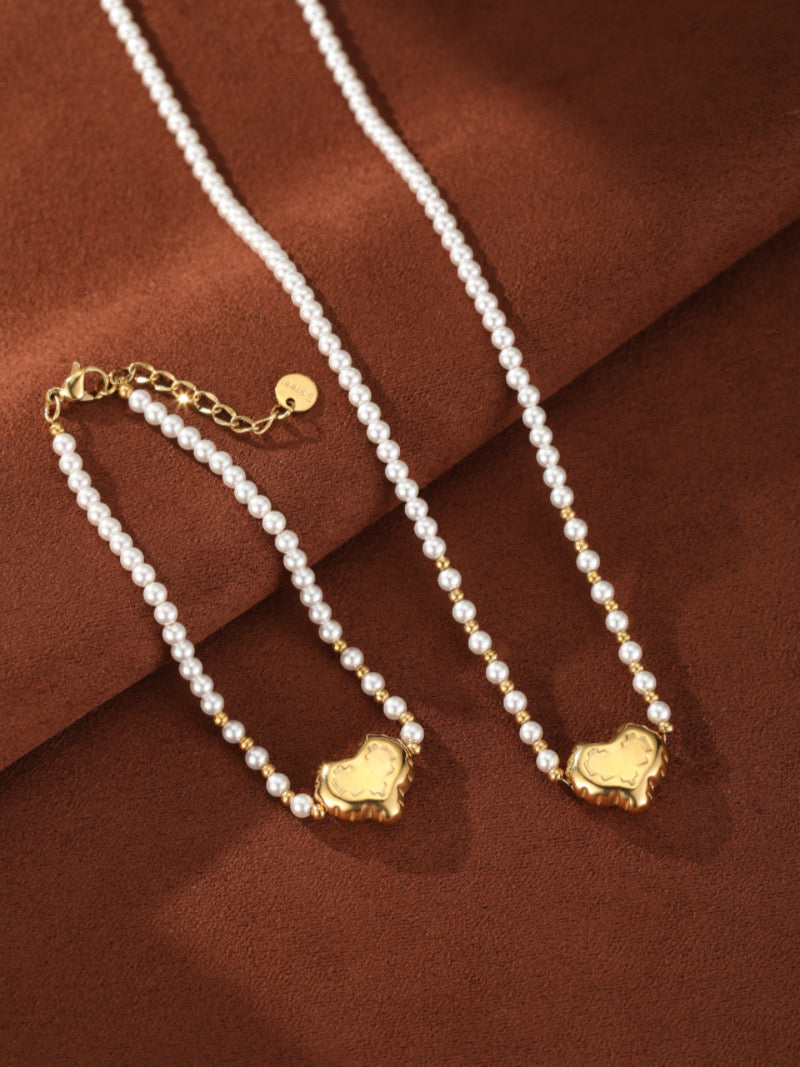 Delicate freshwater pearl beaded bracelet with gold-toned accents and a central puffed heart charm on a brown background.