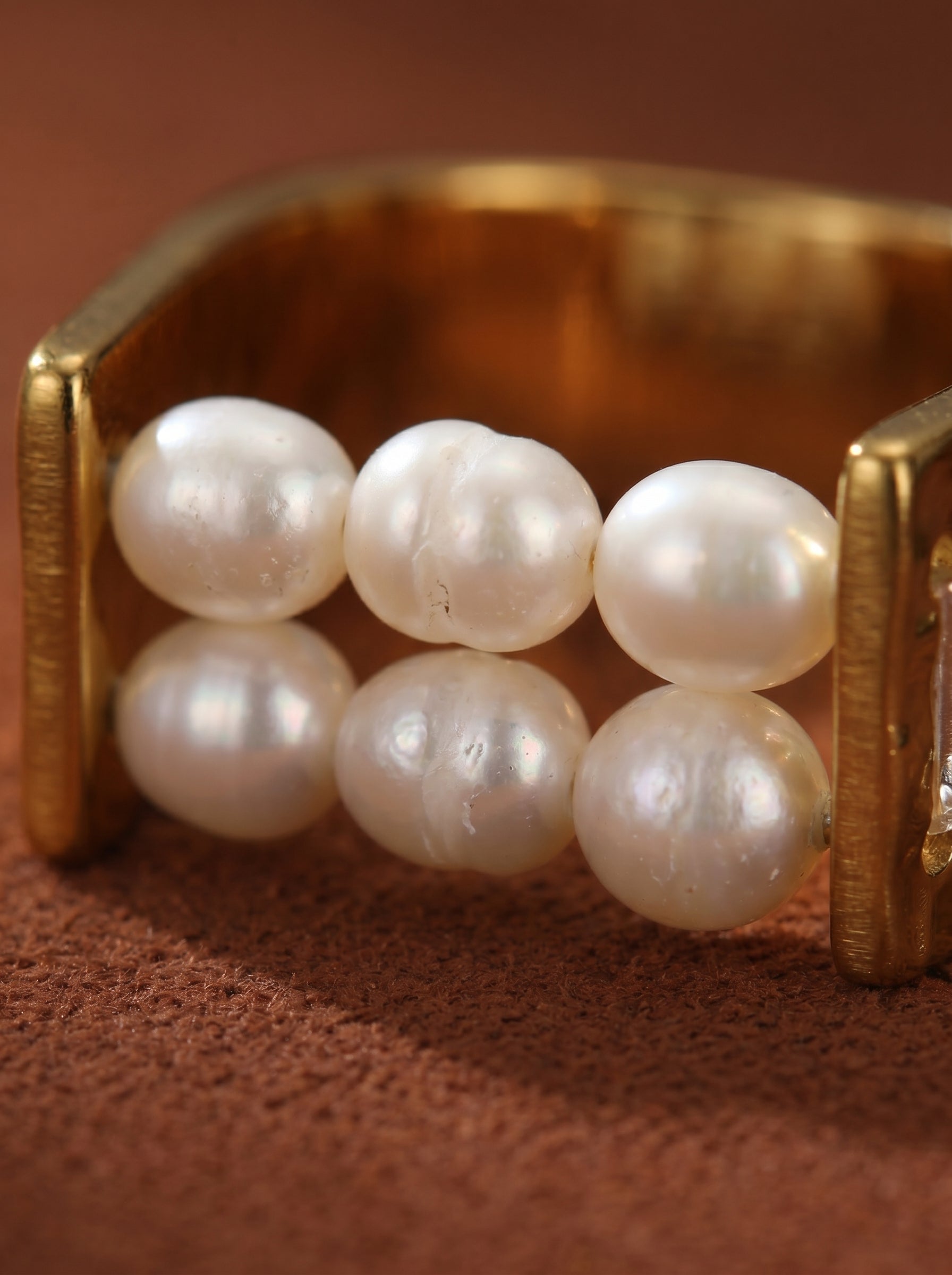 Close-up of the Horizon Freshwater Pearl Beaded Ring, featuring six lustrous seed-shaped white pearls set between polished gold-toned metal bands against a textured brown background. @pearl