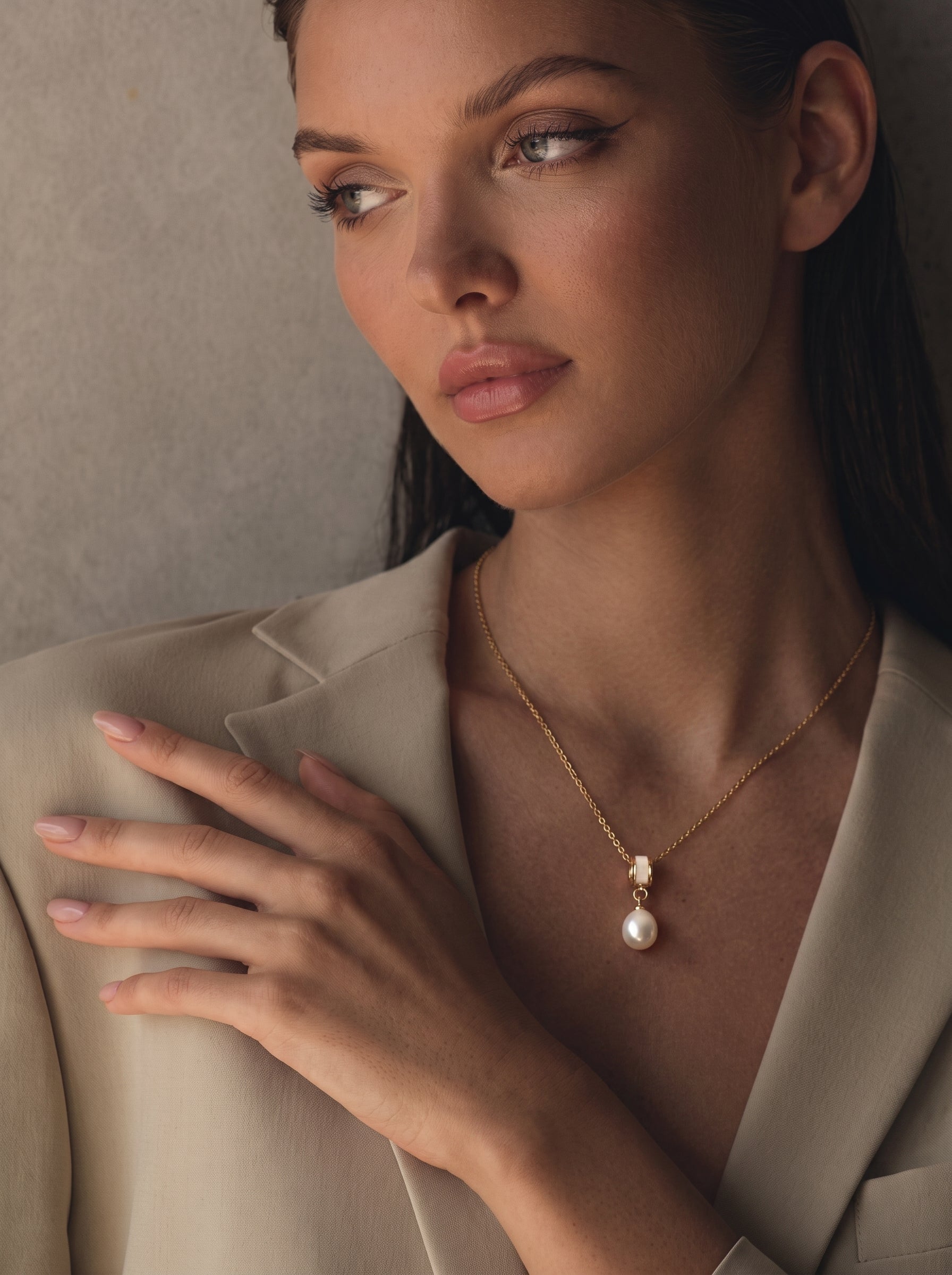 Inner Glow - Collier pendentif goutte en perle d'eau douce sur une femme portant un blazer beige, présentant une seule perle blanche d'eau douce de 8 mm et une chaîne dorée avec un accent cylindrique.@lifestyle