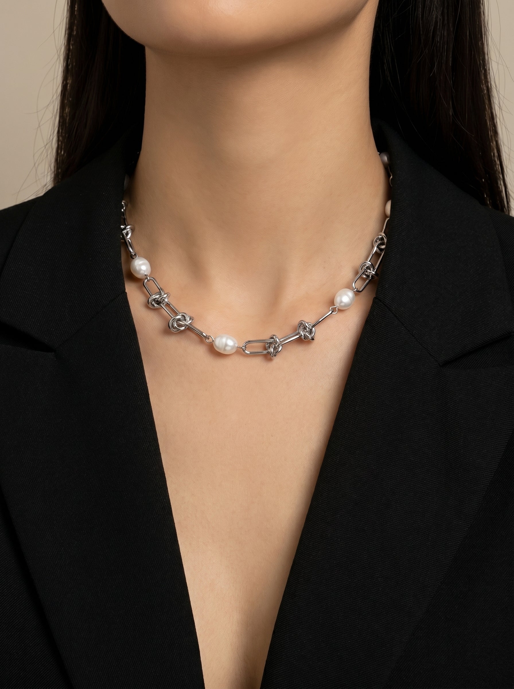 Interlace choker necklace featuring a silver chain with interlinked elements and lustrous white freshwater pearls, worn by a model dressed in a black blazer. @model