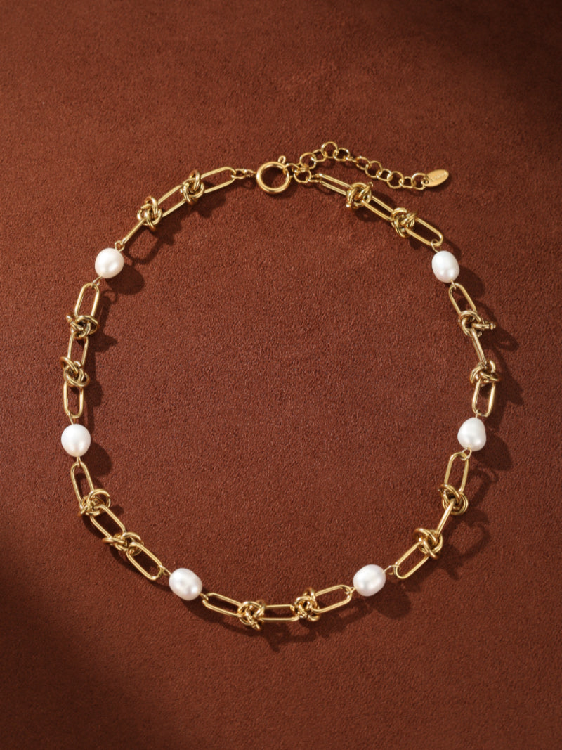 Gold-tone Interlace choker necklace featuring alternating oval links and lustrous white freshwater pearls on a brown background. @pearl
