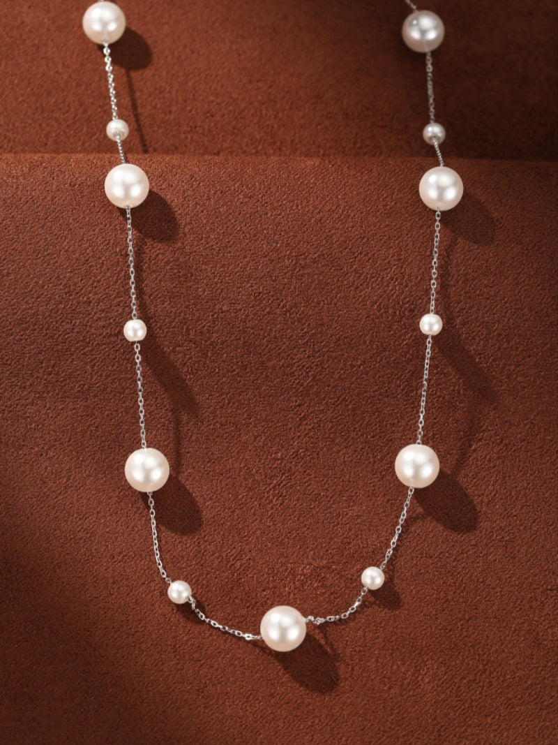 A long silver chain necklace with alternating large and small white imitation pearls on a brown textured background.