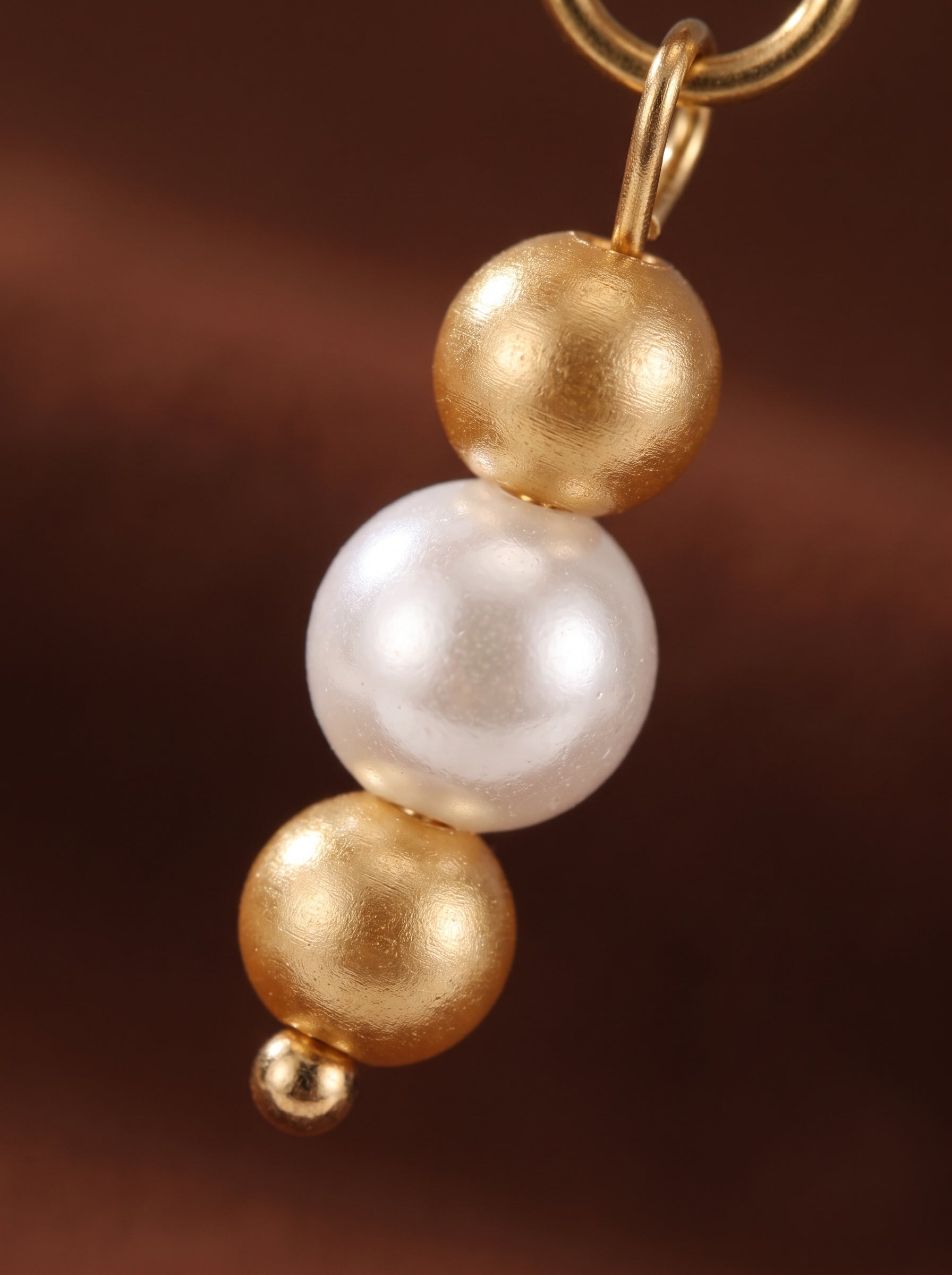 Close-up of a gold hoop earring with a dangle featuring three textured beads: a large white freshwater pearl in the center, flanked by two smaller gold beads above and below. @pearl