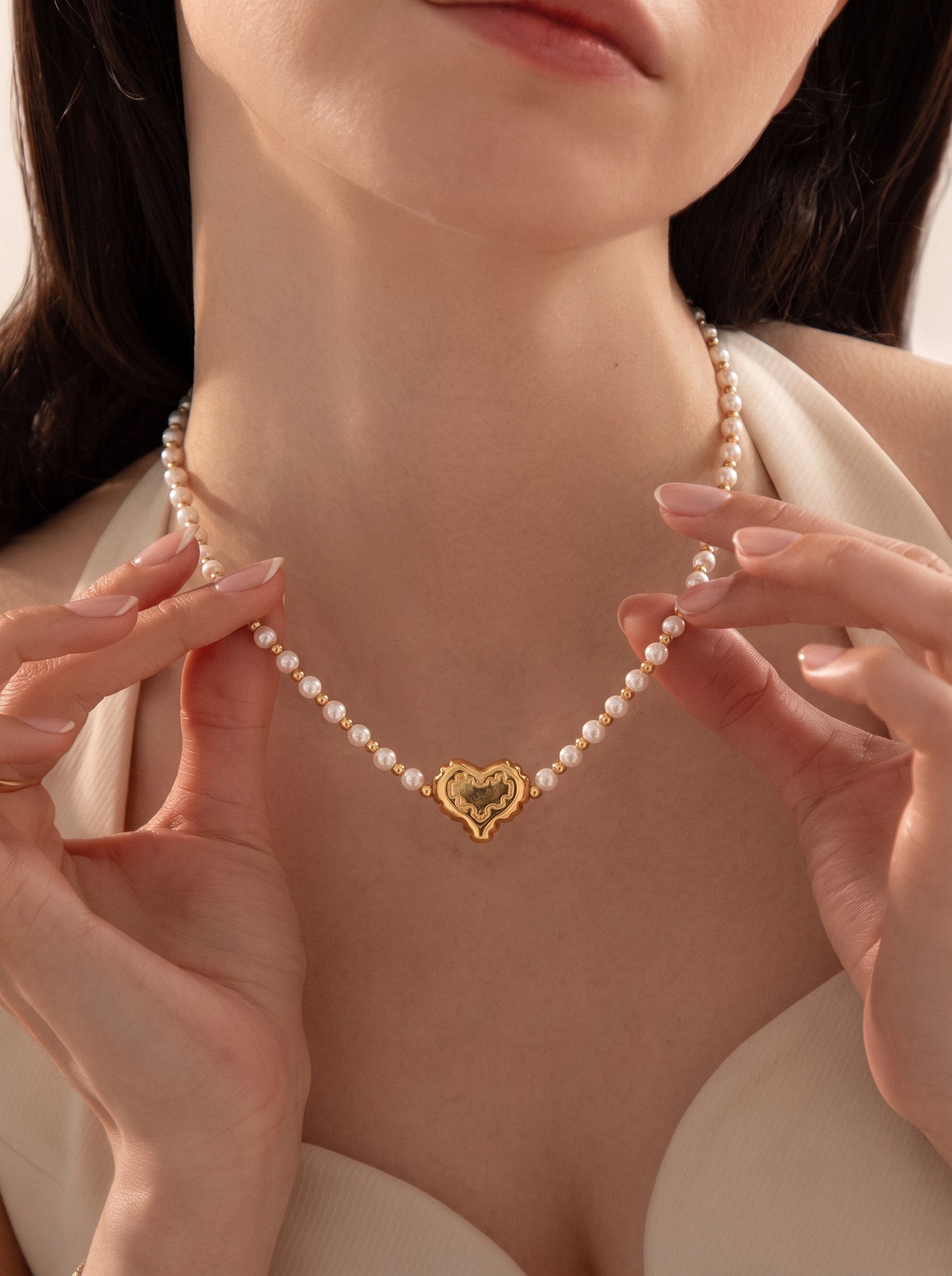 A close-up shot of a woman wearing the Kindred Freshwater Pearl Heart Beaded Pendant Necklace, featuring delicate white pearls and a gold-tone heart pendant. @model