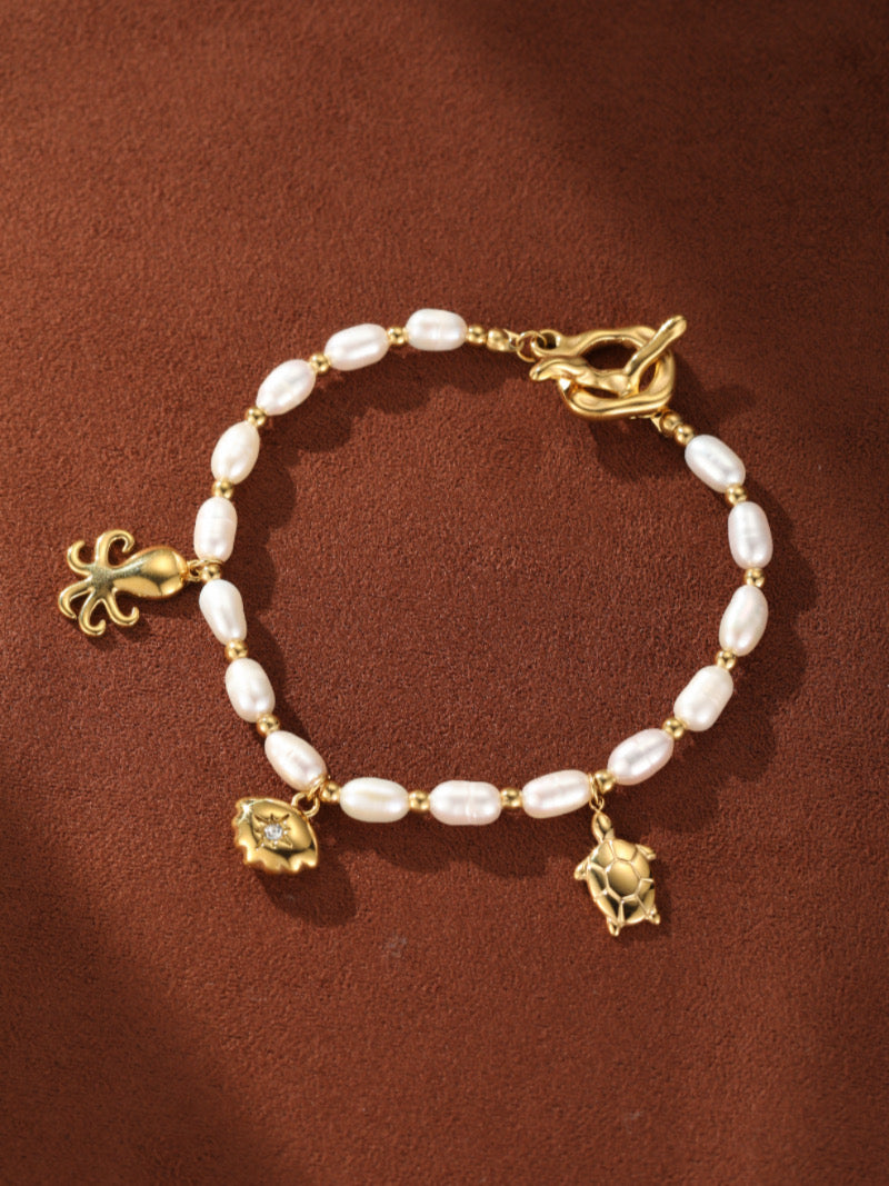 Lagoon bracelet featuring white freshwater seed pearls strung with gold beads, adorned with gold oceanic charms of a turtle, a shell with a diamond accent, and an octopus, fastened with a toggle clasp.
